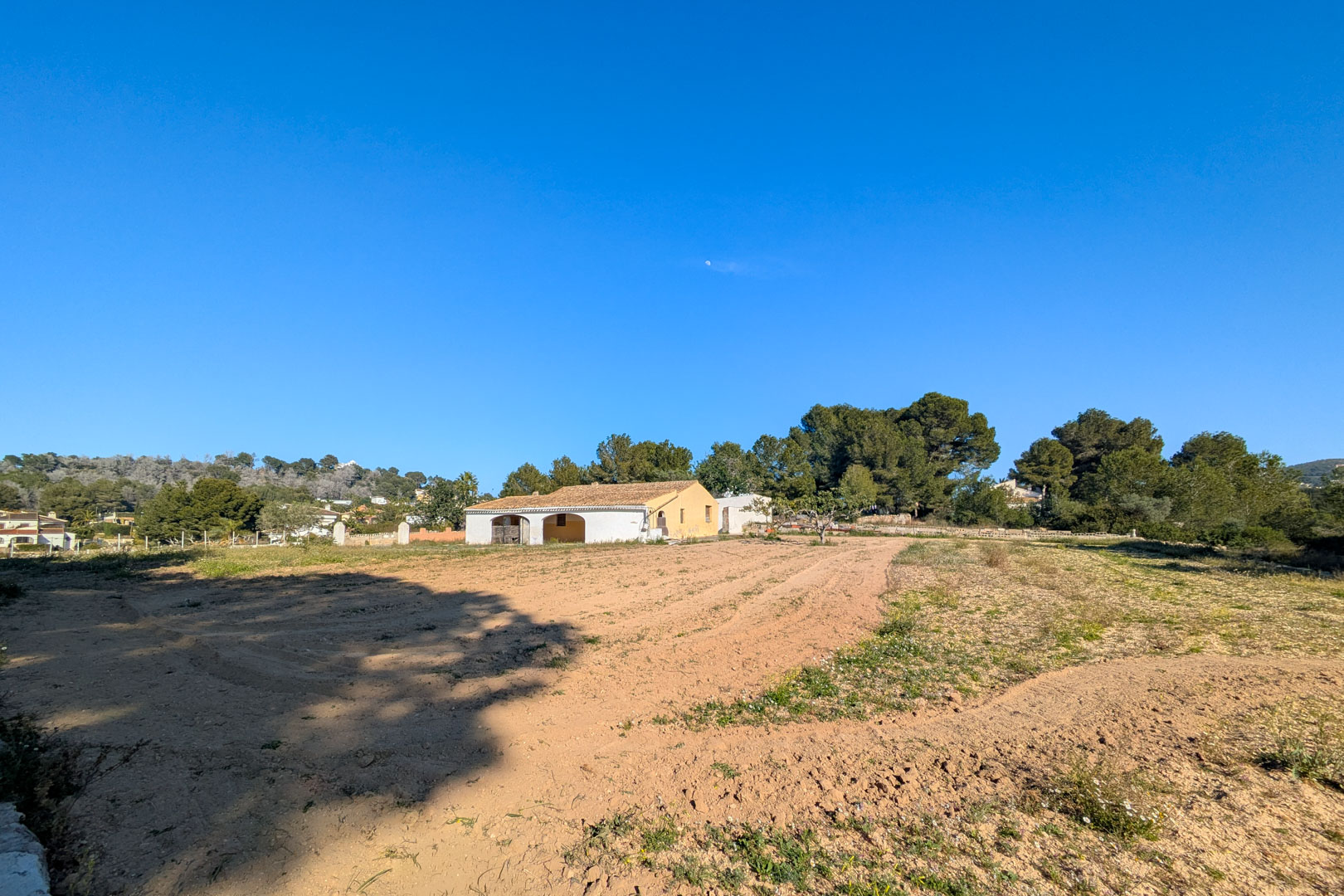 Exterior view of the traditional finca with an arched porch, situated on a large flat rustic plot surrounded by pine trees and natural scenery in Jávea.