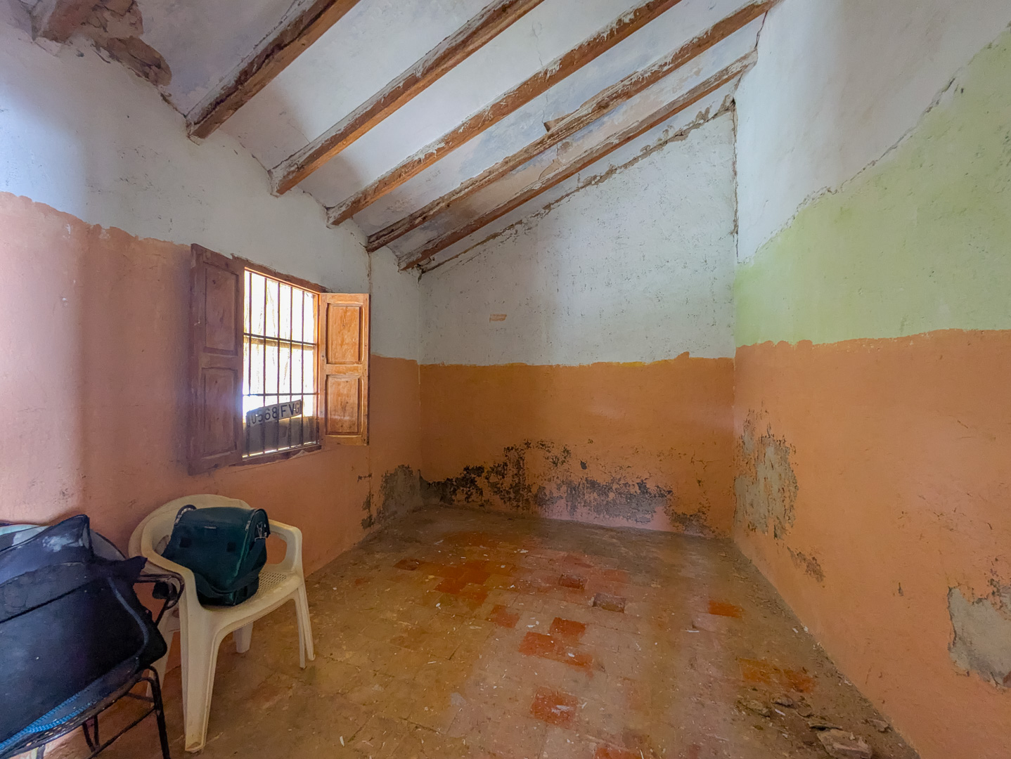 Interior room featuring a sloped ceiling with exposed wooden beams, traditional terracotta tile flooring, and a small window with original wooden shutters.