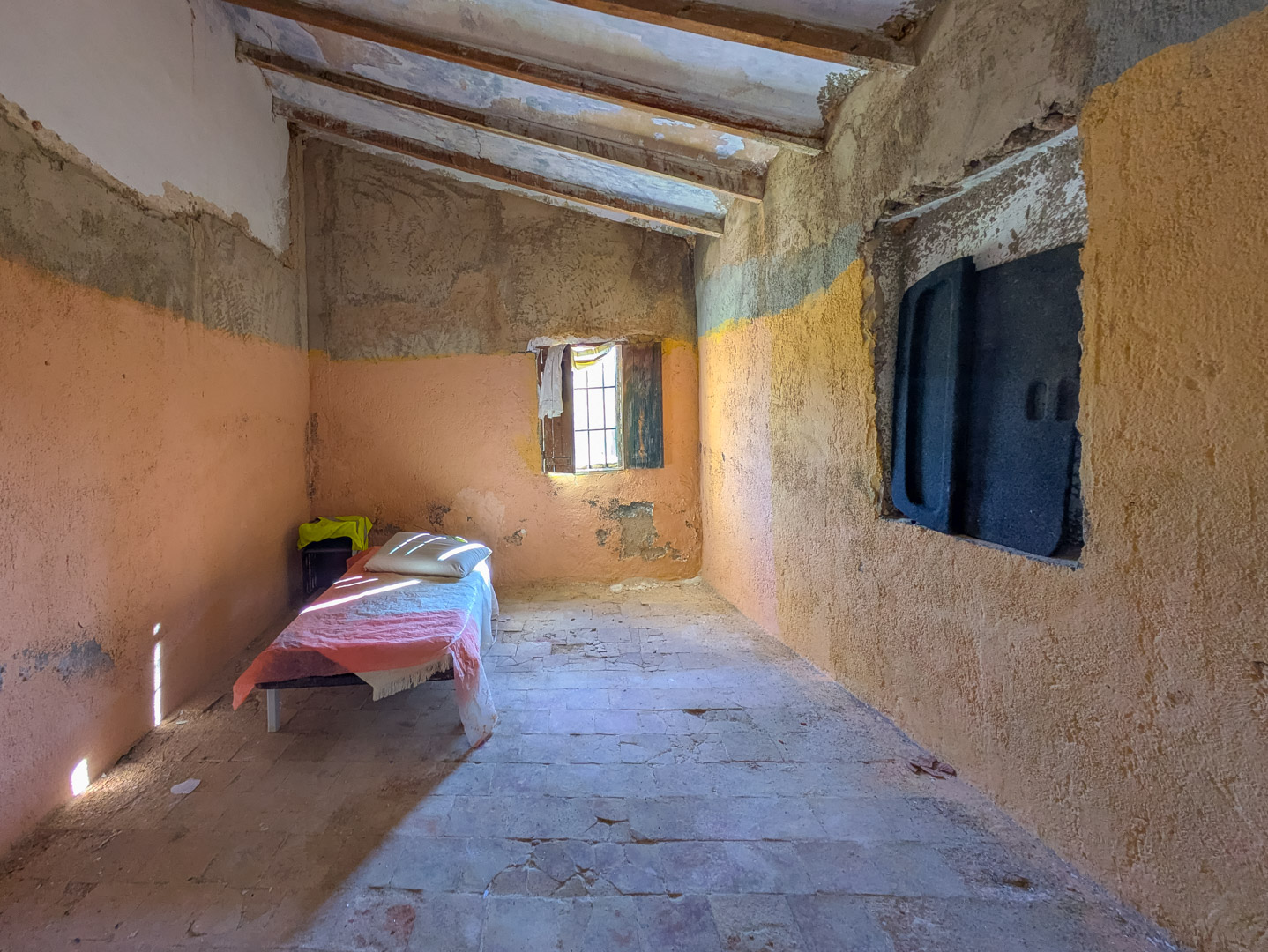 Interior room featuring sloped ceilings with exposed wooden beams, original terracotta tile flooring, and rustic plastered walls awaiting complete restoration.
