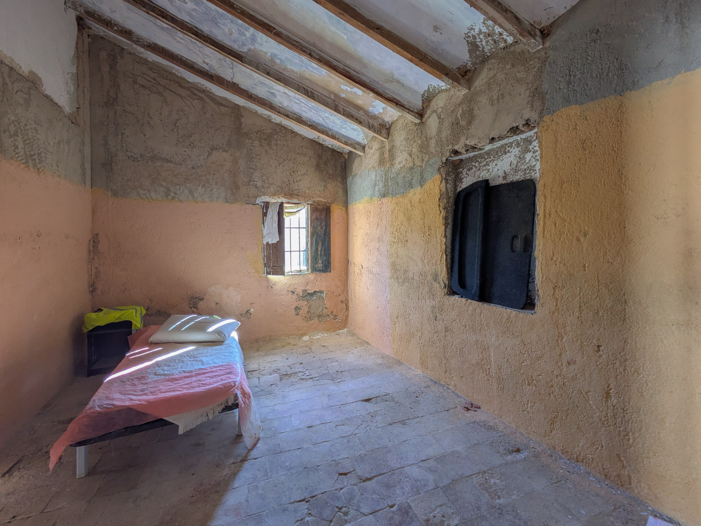 Rustic interior featuring exposed wooden ceiling beams, original terracotta flooring, and textured walls ready for complete renovation.