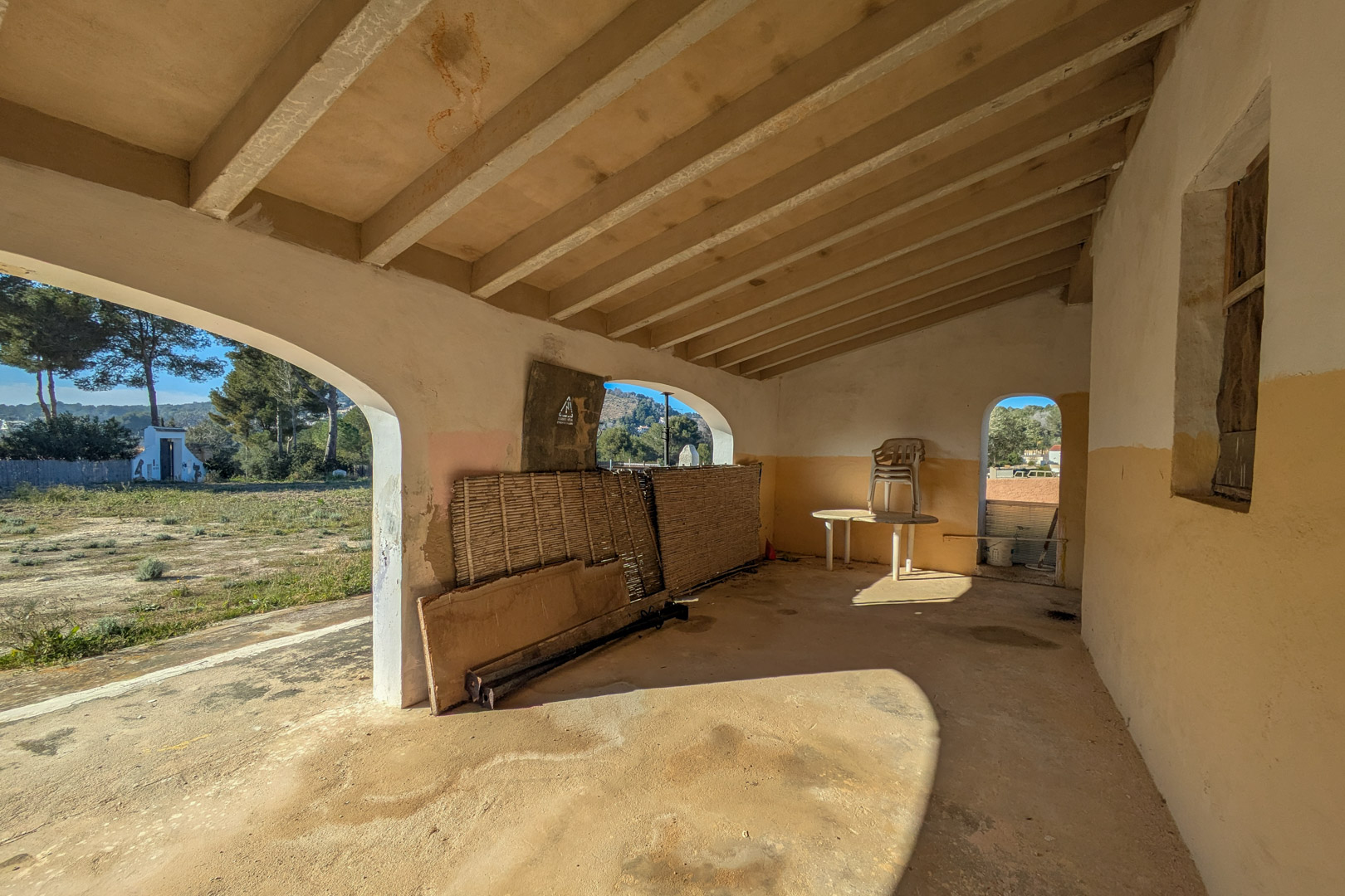 Traditional covered porch featuring exposed ceiling beams and arched openings overlooking the expansive rustic plot and natural surroundings.