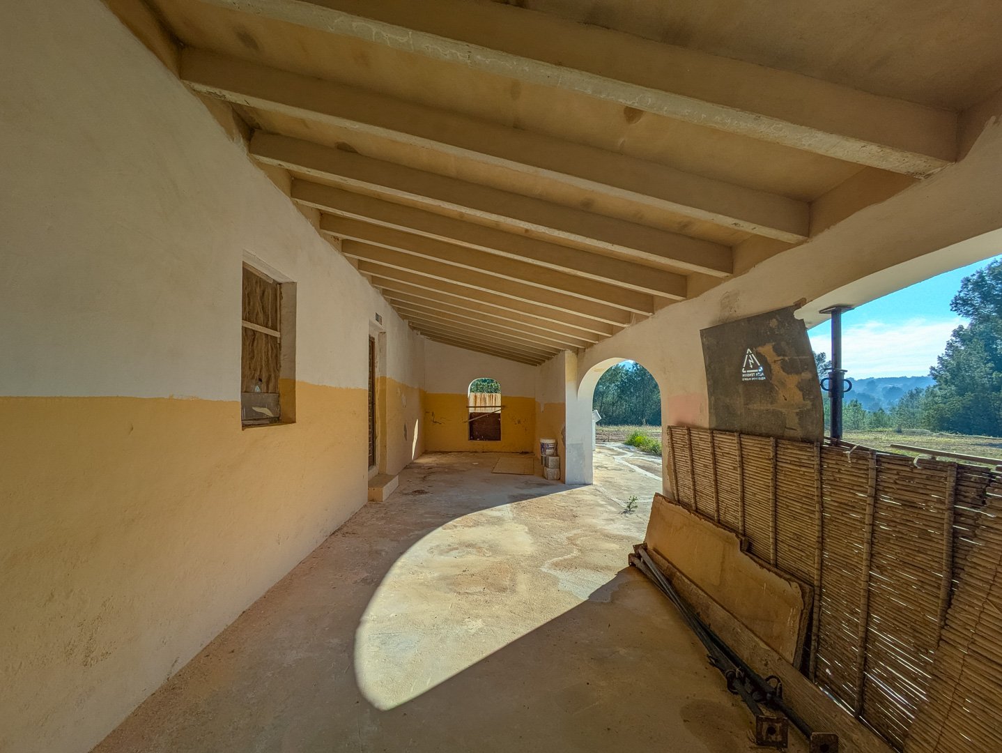 Traditional covered porch featuring exposed wooden ceiling beams and ochre-toned walls, overlooking the natural landscape of Jávea.