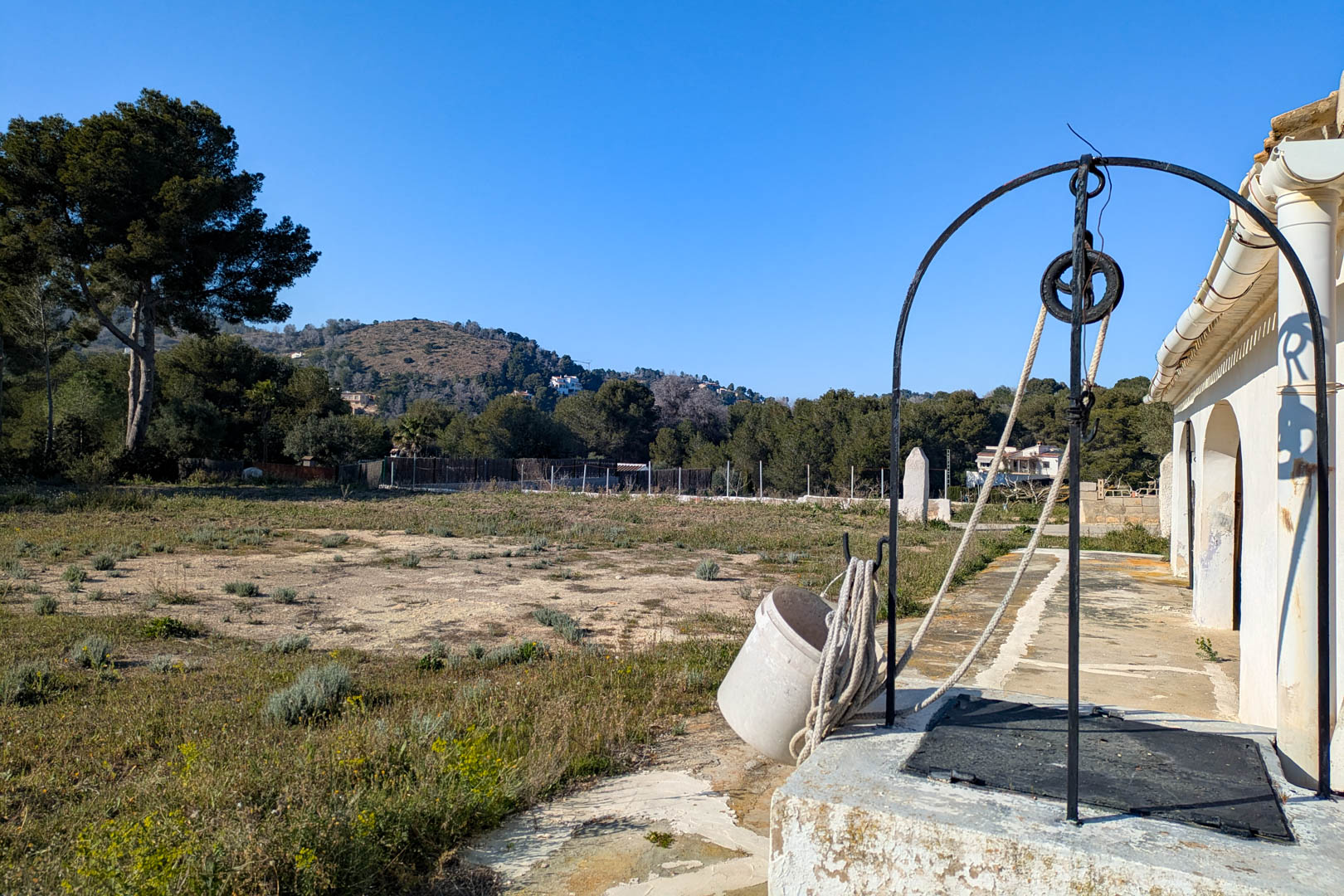 Traditional water well with a wrought iron arch and pulley system, located on the expansive rustic plot with clear views of the Mediterranean hills.
