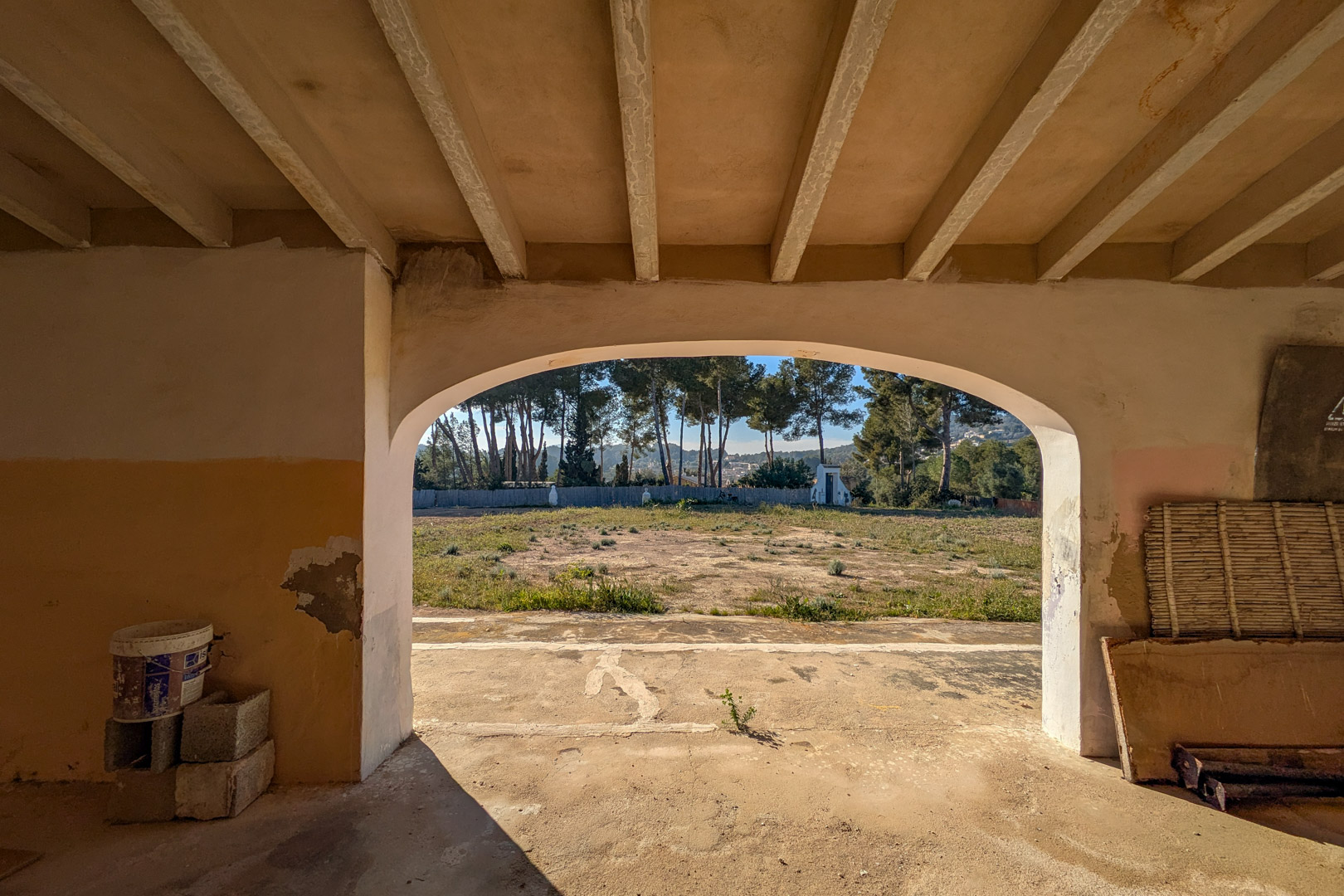 View from inside an arched porch featuring beamed ceilings, overlooking the expansive rustic plot and a perimeter of mature pine trees.