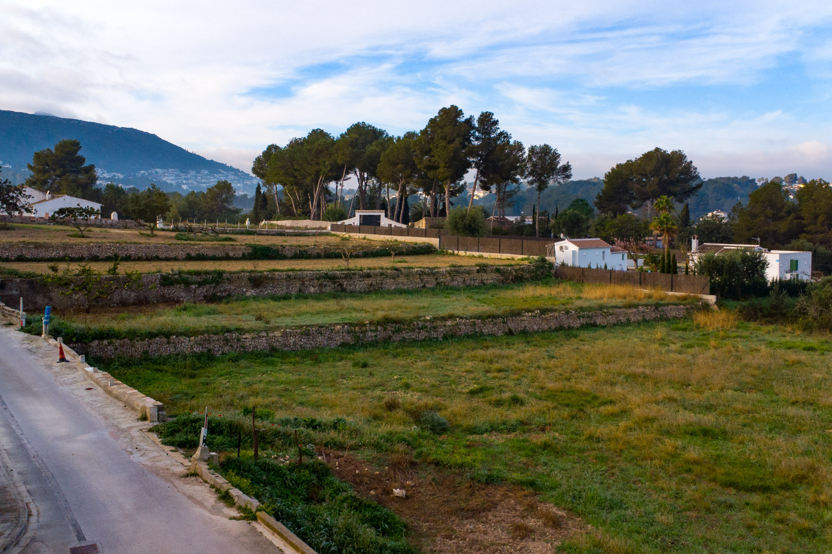 View of the dry stone terraces on the expansive rustic plot, surrounded by Mediterranean vegetation with mountain views in the distance.