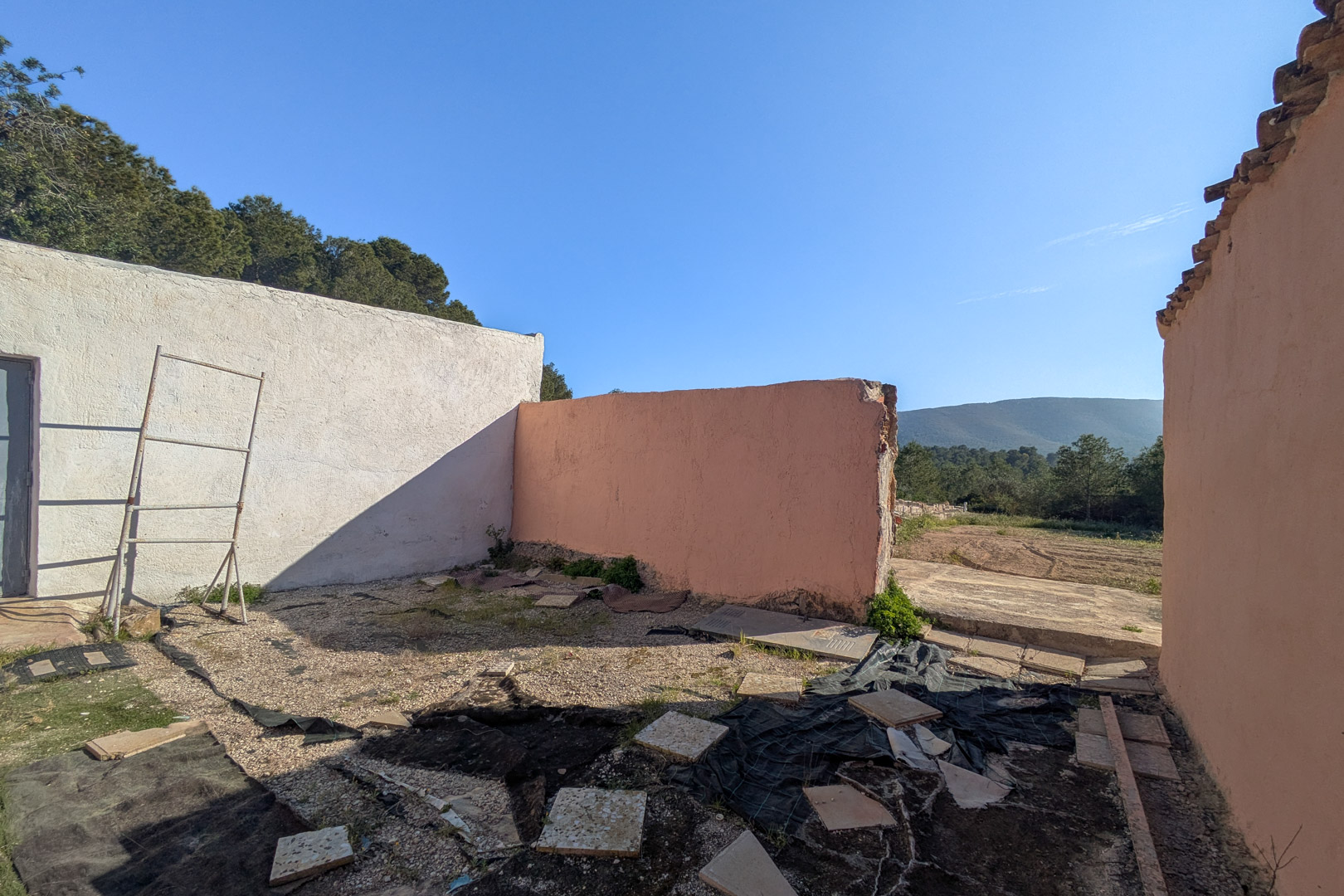 View of the outdoor structure featuring textured walls in white and terracotta, overlooking the natural landscape and distant mountains under a clear sky.