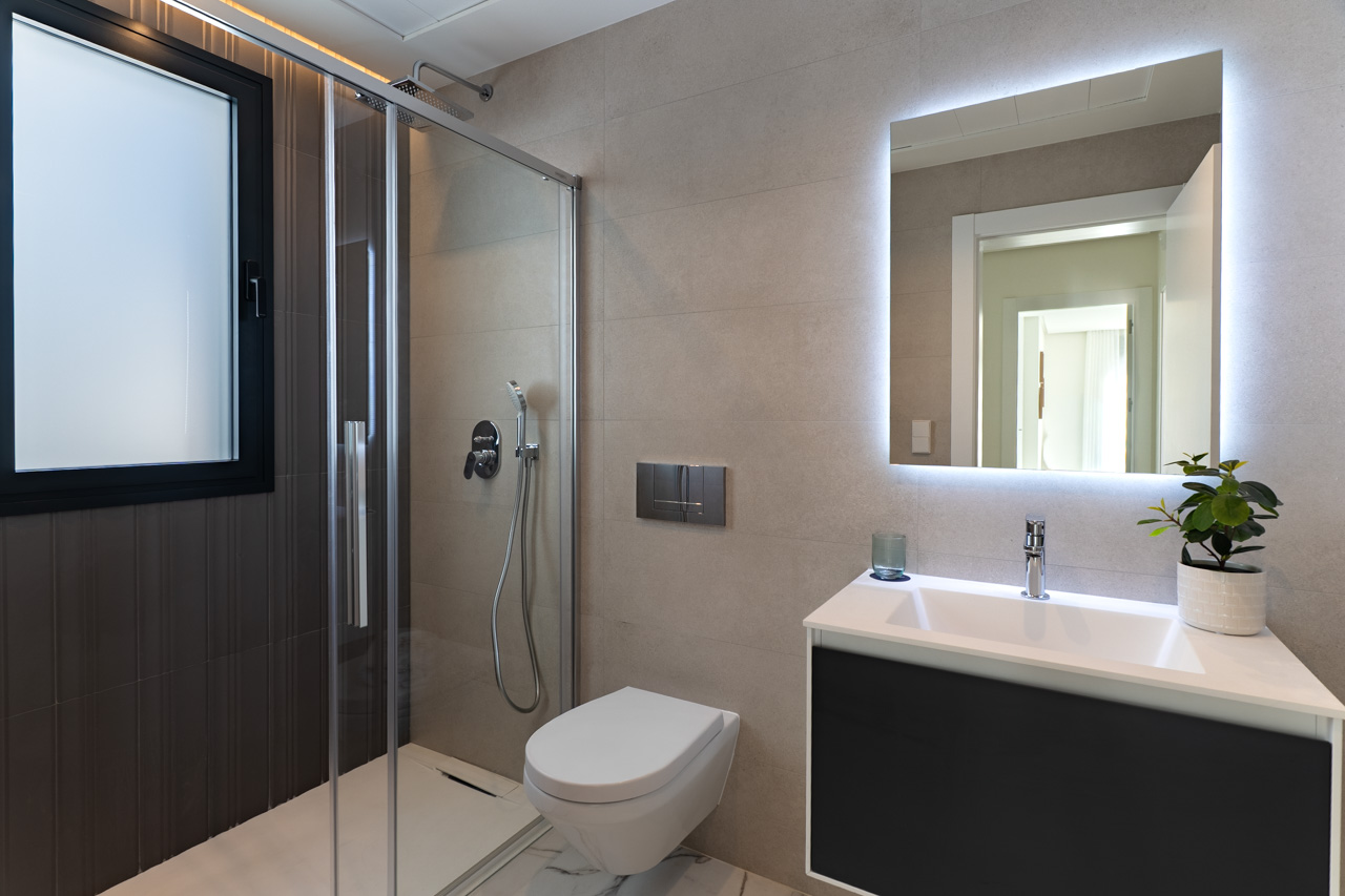 Contemporary bathroom featuring a walk-in shower with glass screen, wall-mounted toilet, and a sleek vanity unit with an integrated LED back-lit mirror.