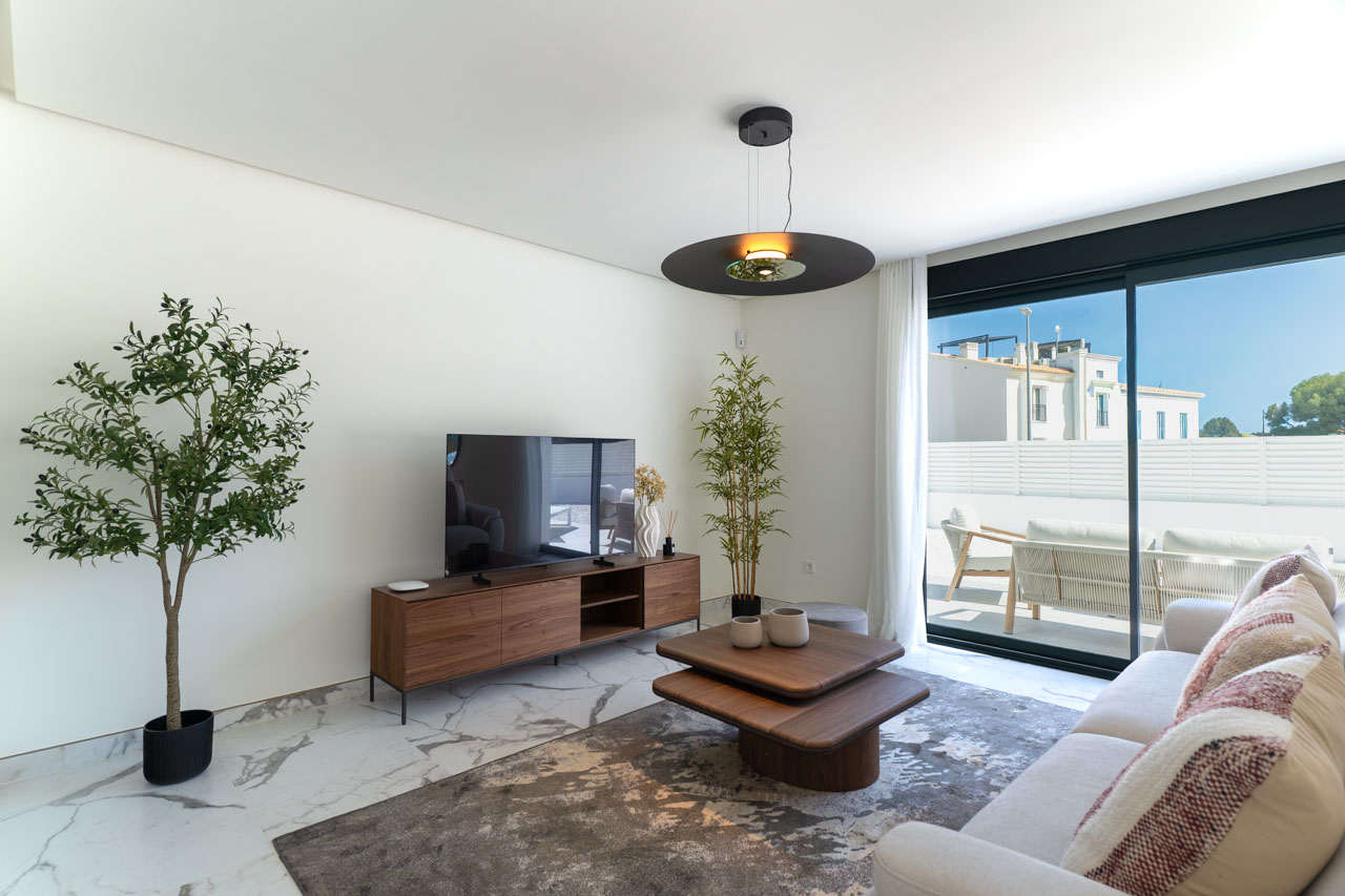 Contemporary living room featuring marble-effect flooring, wooden minimalist furniture, and large sliding glass doors opening onto a private sun terrace.
