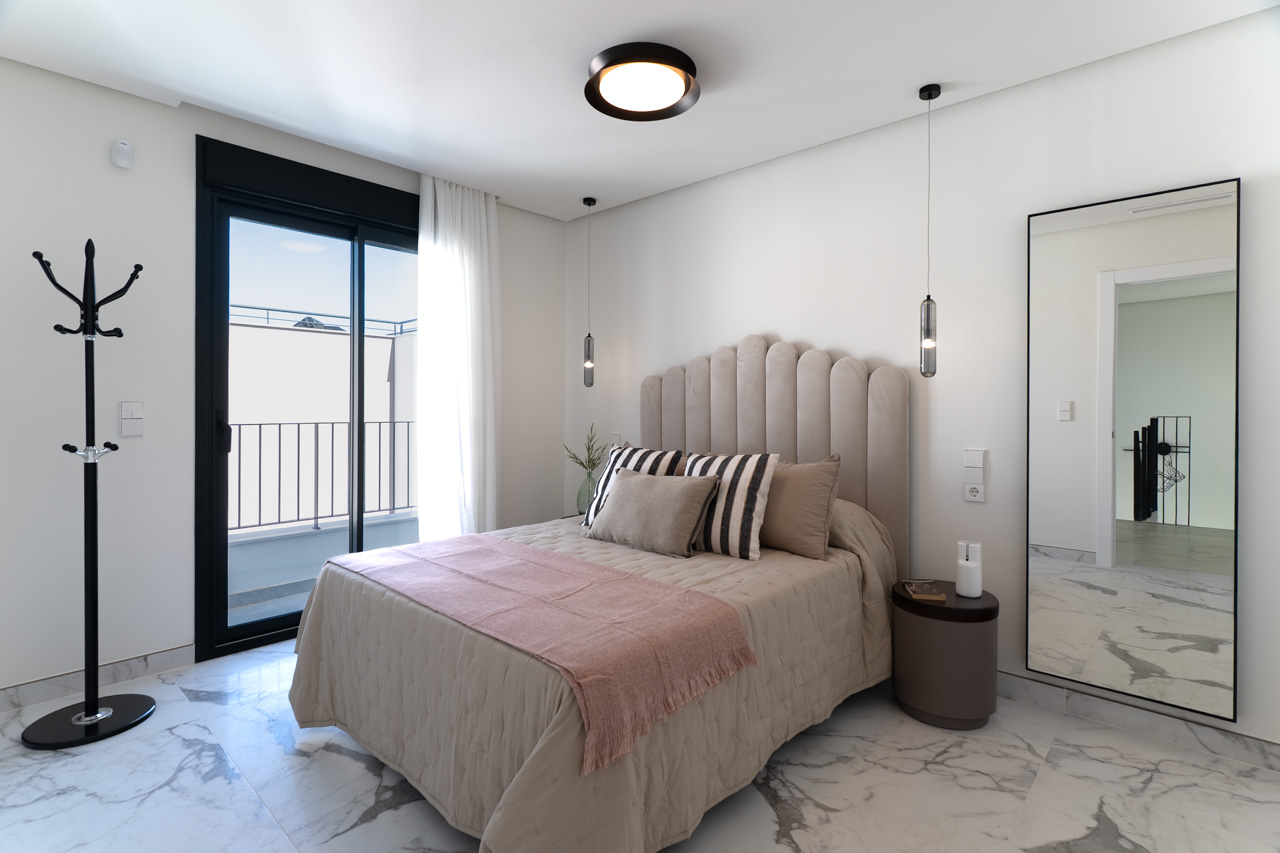 Double bedroom featuring marble-effect porcelain flooring, a scalloped upholstered headboard, and direct access to a private balcony through black-framed sliding doors.