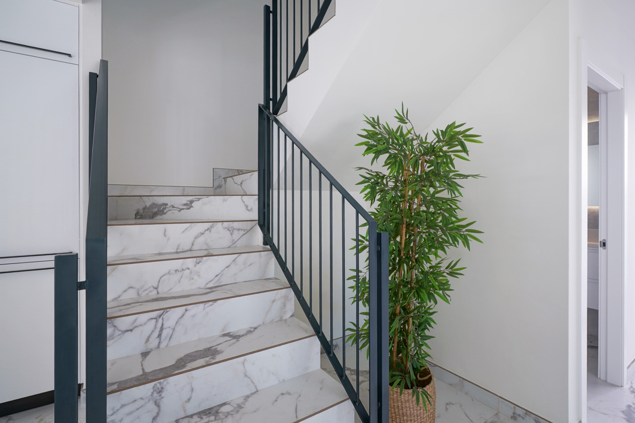 Interior staircase featuring marble-effect porcelain steps and a minimalist black metal railing, connecting the levels with a clean, contemporary design.