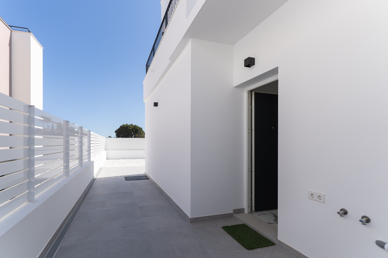 Main access and exterior side path with grey ceramic tiling, smooth white walls, and slatted perimeter fencing, highlighting the modern linear architecture.