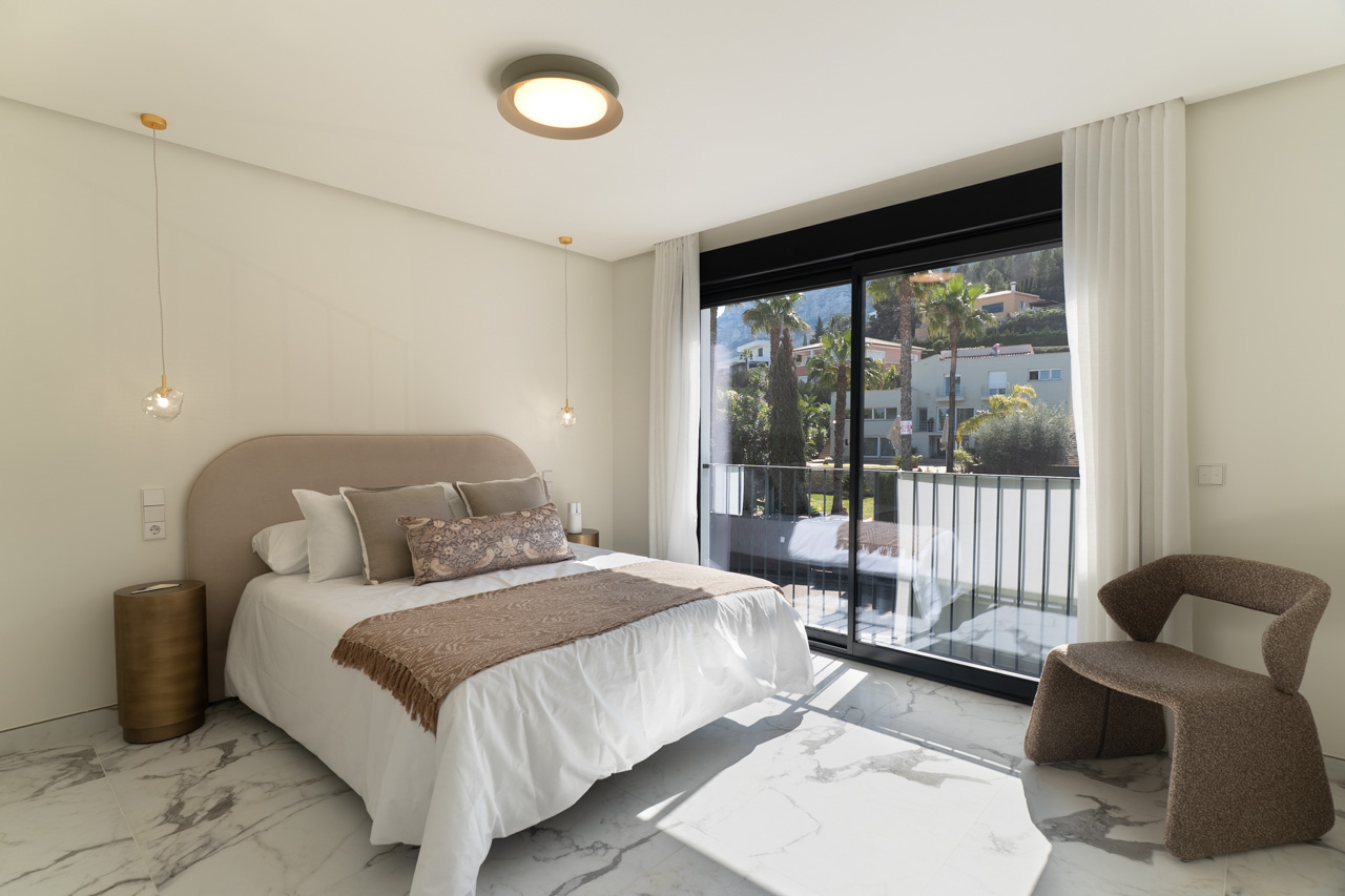 Master bedroom featuring marble-effect porcelain floors and floor-to-ceiling sliding glass doors opening onto a private balcony with views.