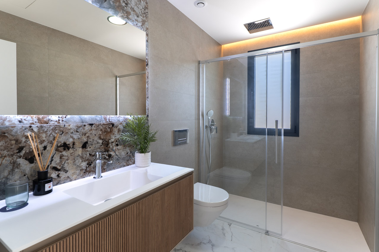 Modern bathroom featuring a slatted wood vanity, marble-effect backsplash, and a walk-in shower with glass partition and recessed lighting.