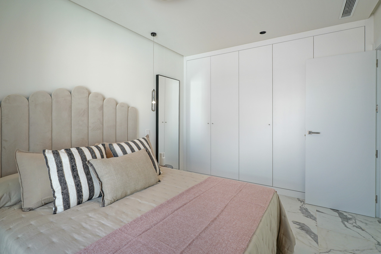 Modern bedroom featuring floor-to-ceiling white wardrobes, veined marble flooring, and a decorative scalloped headboard with minimalist pendant lighting.