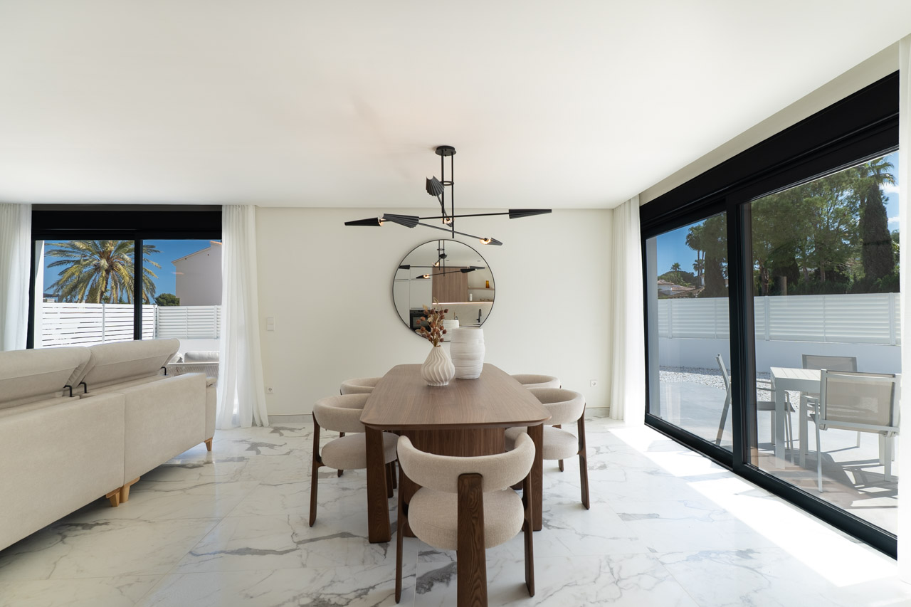 Open-plan dining area featuring a wooden table, designer lighting, and marble-effect flooring. Large sliding doors provide direct access to the terrace.