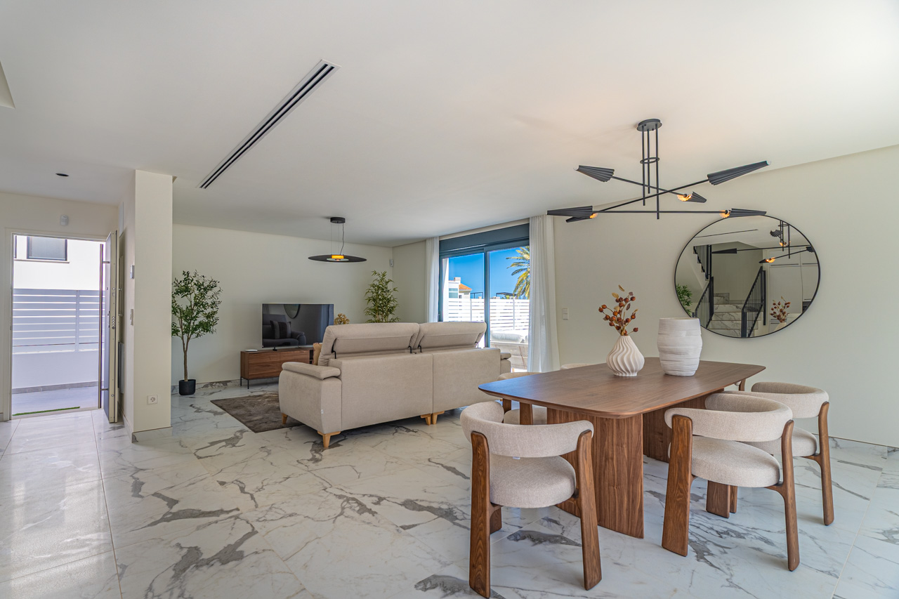 Open-plan living and dining area featuring marble-effect porcelain flooring, contemporary wooden furniture, and large glass doors leading to the exterior.