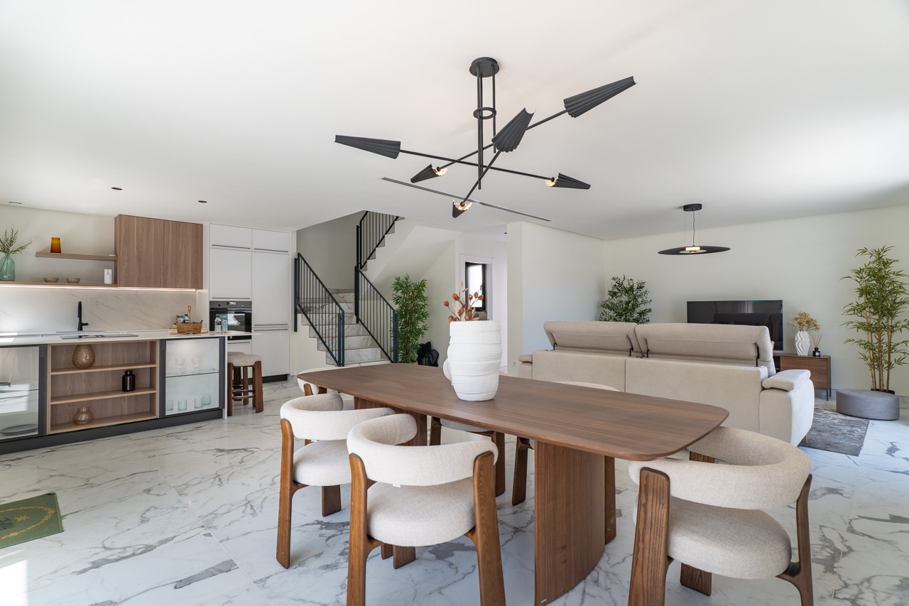 Open-plan living area featuring a wood dining set, a modern kitchen with marble-effect finishes, and a minimalist staircase with black metal railings.