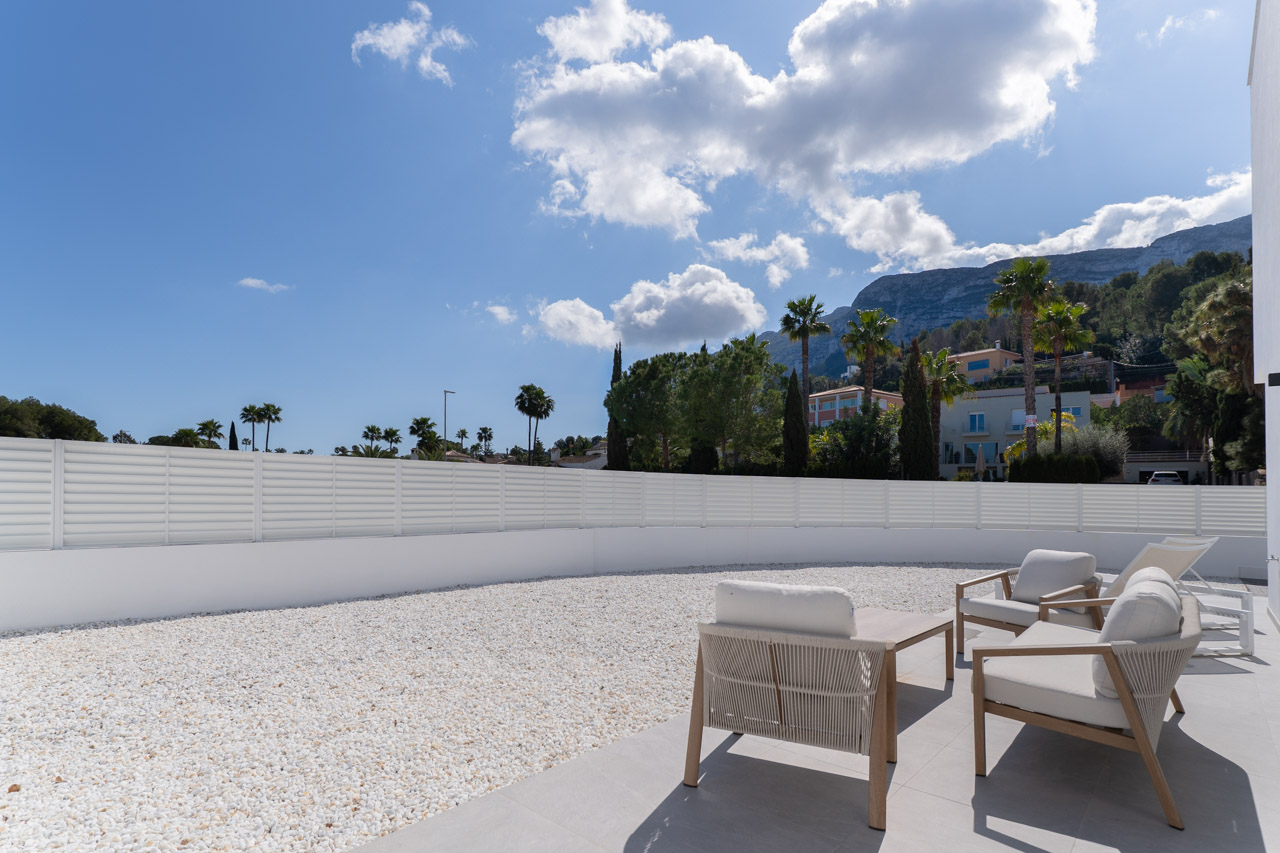 Outdoor terrace with modern lounge seating, a white gravel perimeter, and clear views of the Montgó mountain under a bright sky.