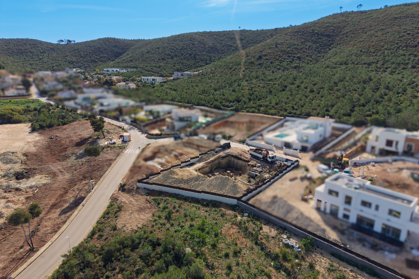 Aerial view of the construction site showing the excavation and foundation phase for a modern villa in the green Valsol residential area.