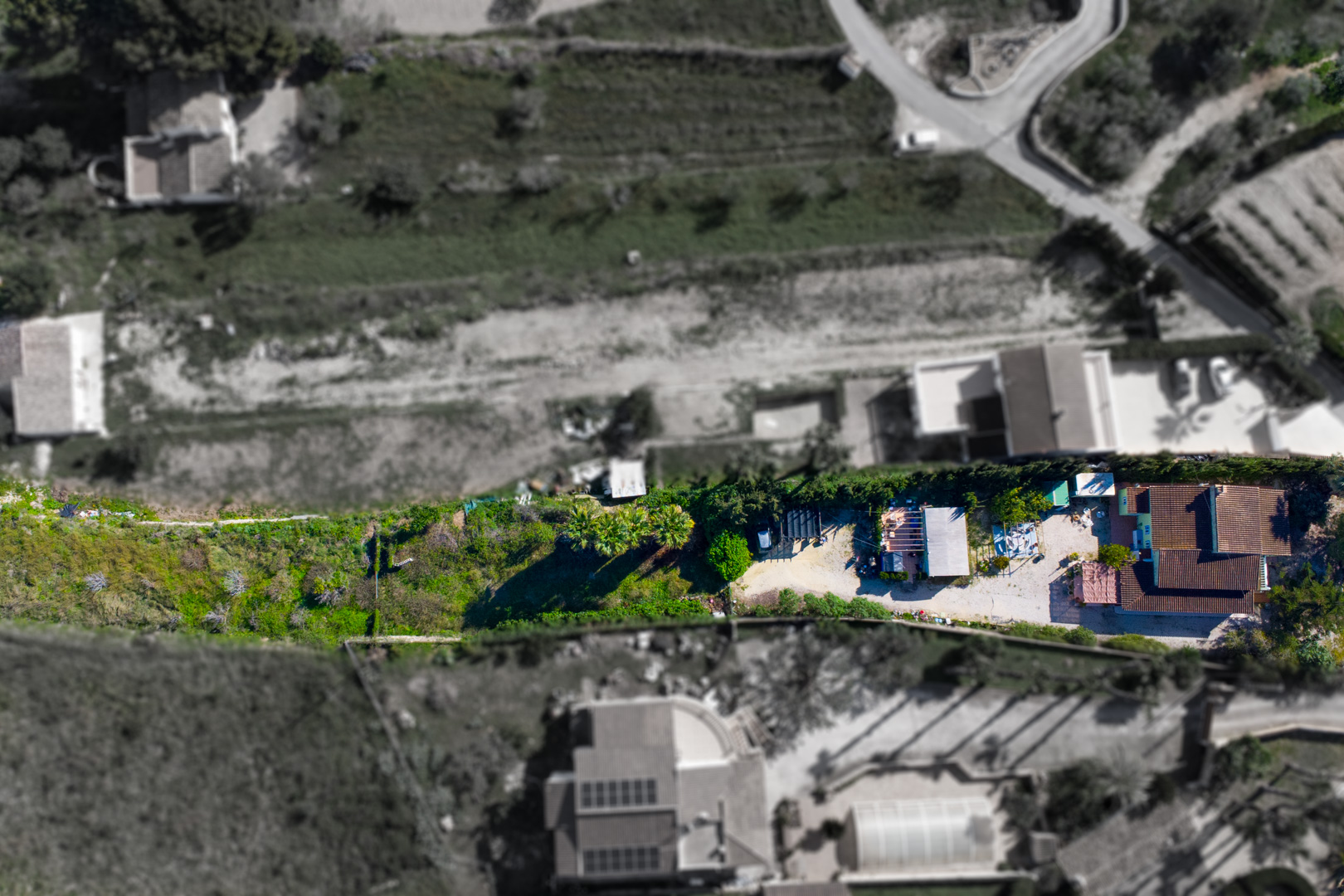 Aerial bird's-eye view showing the layout of the main villa, the auxiliary prefab building, and the expansive rustic plot situated on the valley ridge.