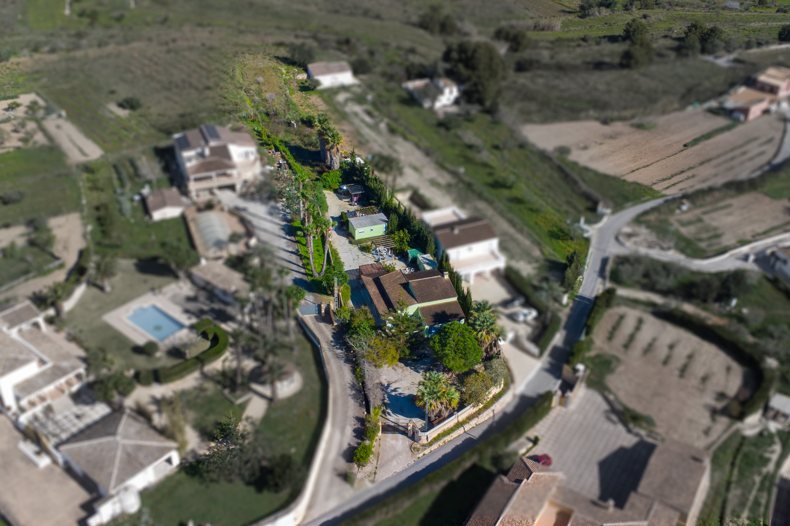 Aerial view of the 2,800 m2 rustic plot featuring the main villa, a separate pre-fabricated unit, and a long driveway lined with Mediterranean vegetation.