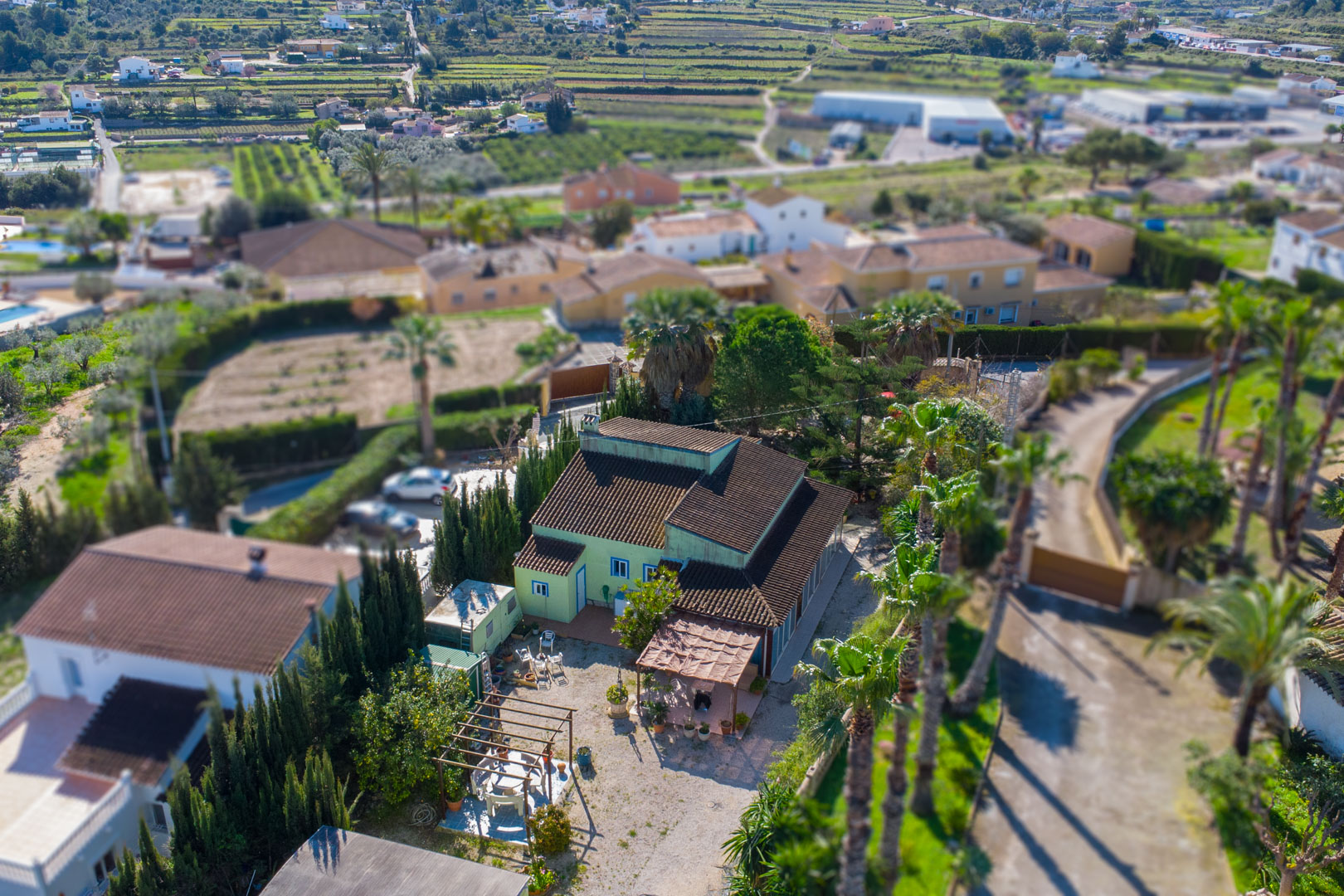 Aerial view of the traditional villa featuring a green facade, tiled roof, and outdoor living areas with wooden pergolas amidst a Mediterranean landscape.