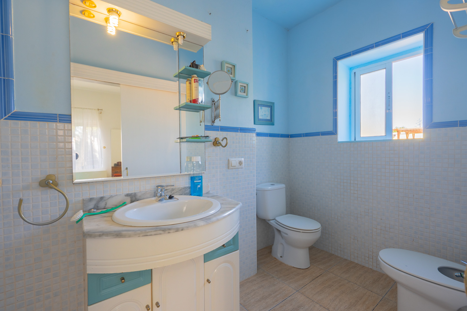 Bathroom featuring blue and white mosaic tiling, a marble-topped vanity with integrated sink, and natural light from a side window.