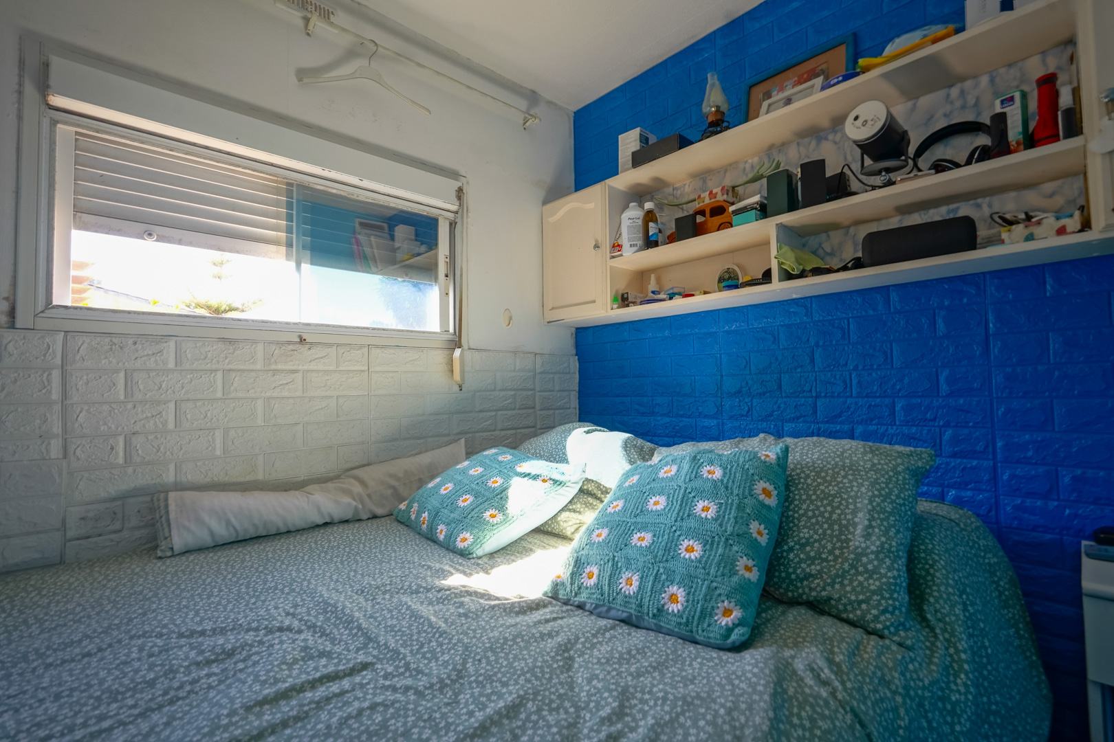 Bedroom in the prefabricated unit featuring blue and white brick-effect walls, integrated shelving, and natural light.