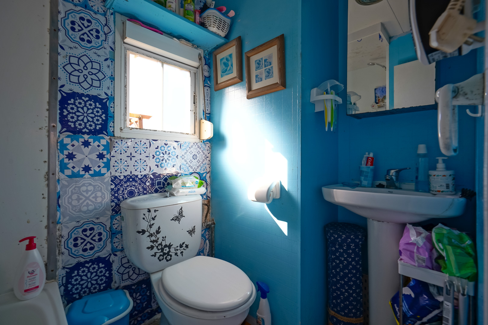 Compact bathroom featuring blue walls, decorative patterned tiling, a pedestal sink, and a small window providing natural light.