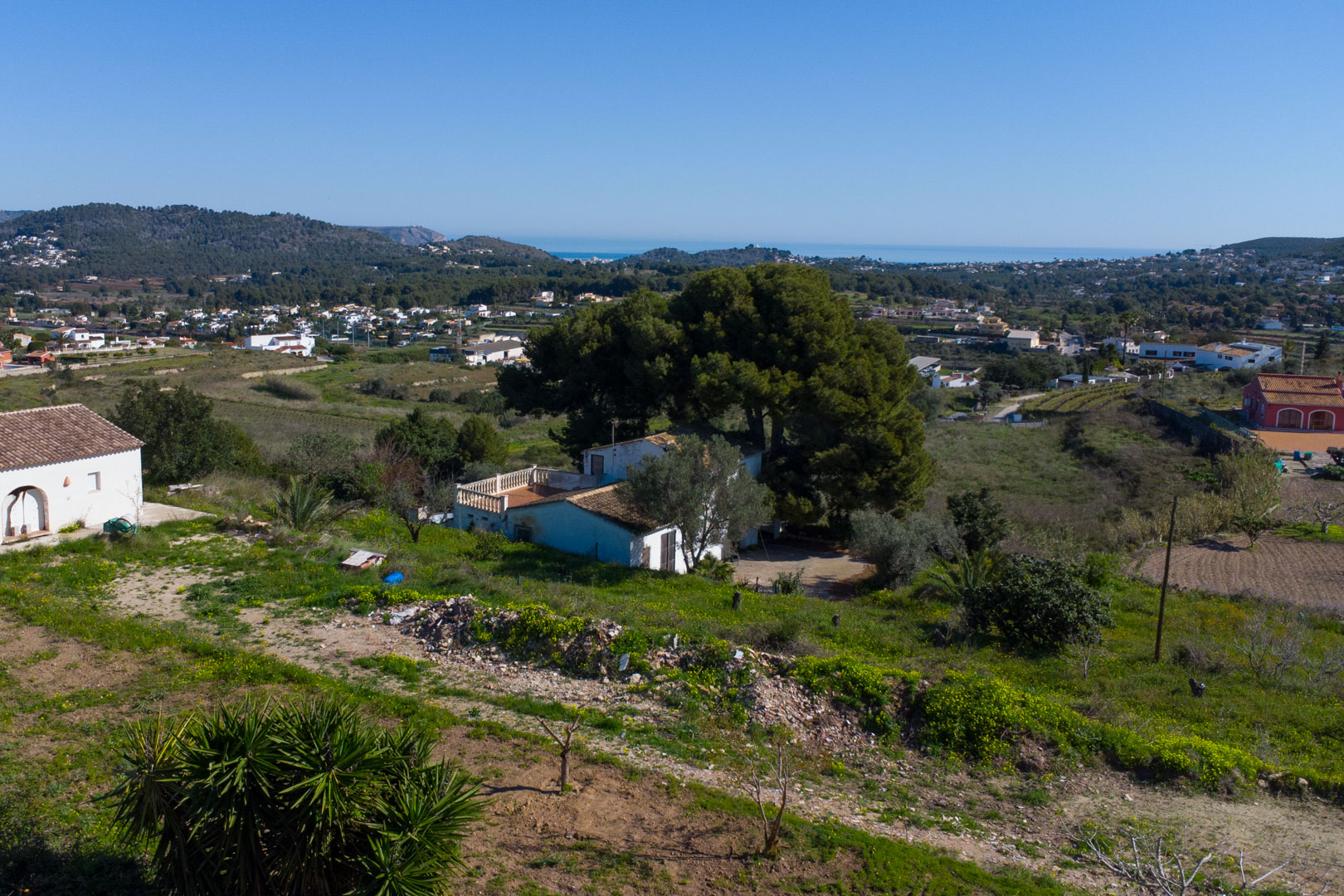 Elevated view of the traditional finca and its rustic plot, featuring panoramic vistas across the Benitachell valley towards the Mediterranean Sea.