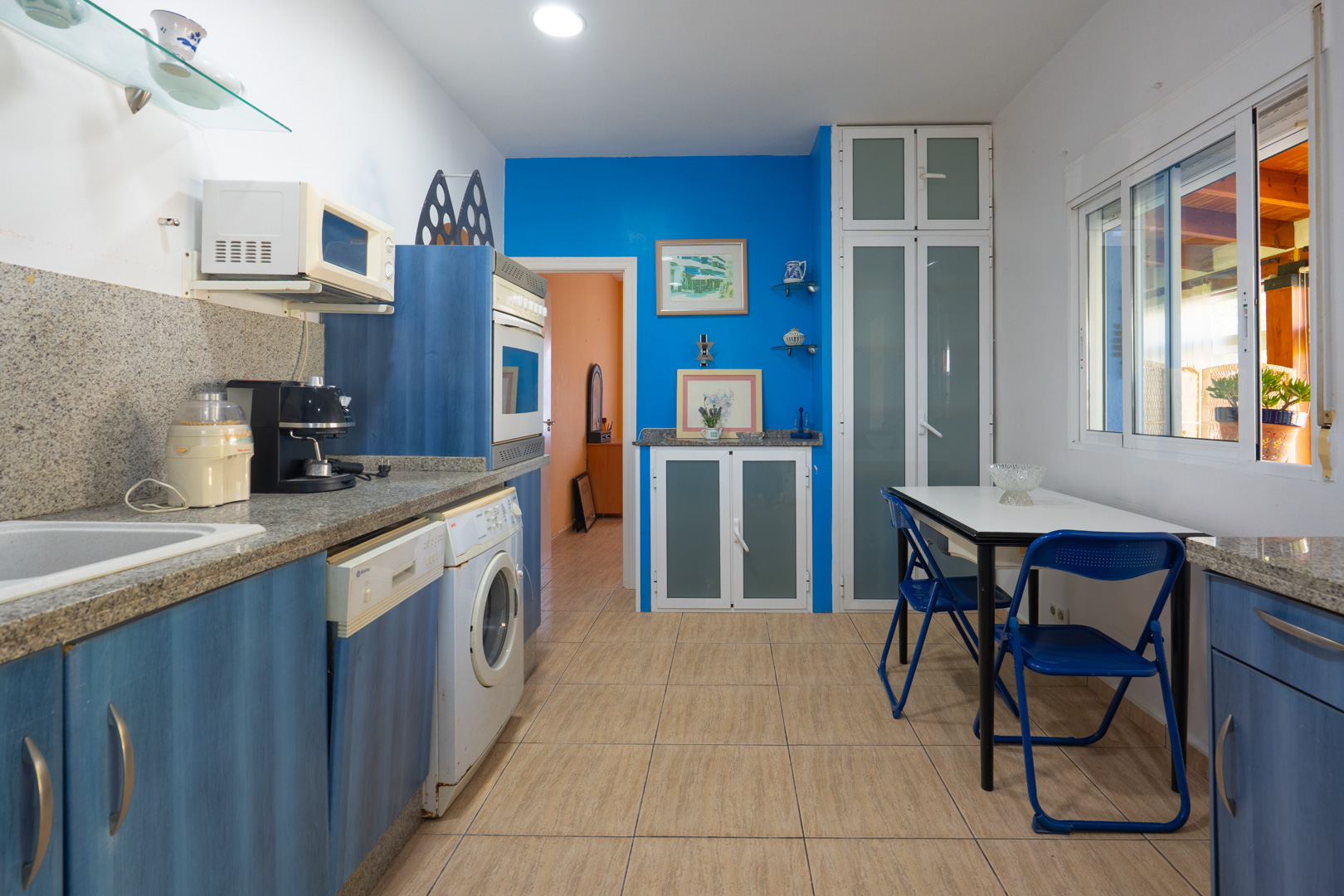 Equipped kitchen with blue cabinetry, grey granite countertops, a breakfast nook, and integrated appliances under recessed lighting.