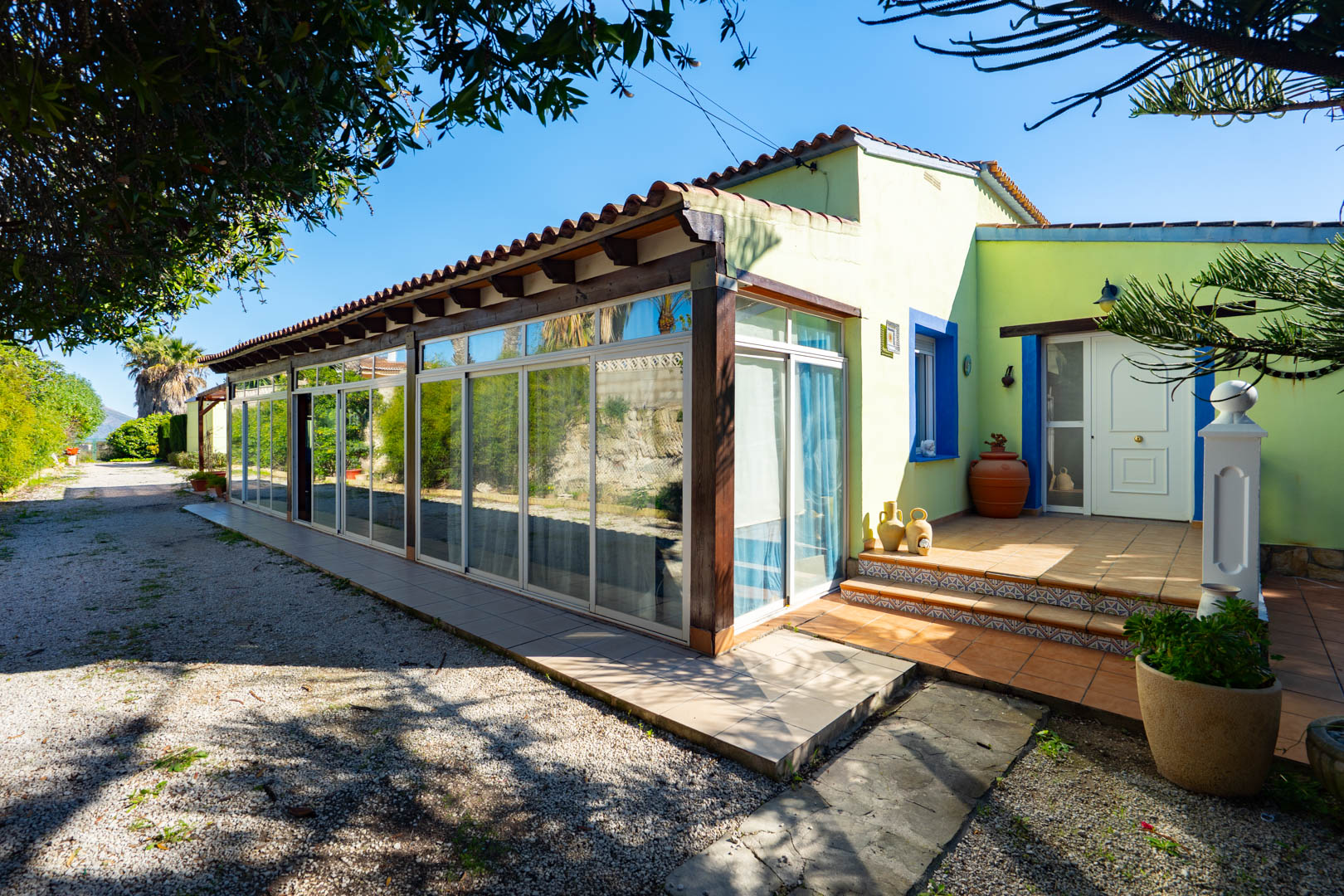Finca exterior featuring a glass-enclosed naya with wooden beams and a tiled entrance porch with Mediterranean blue accents.