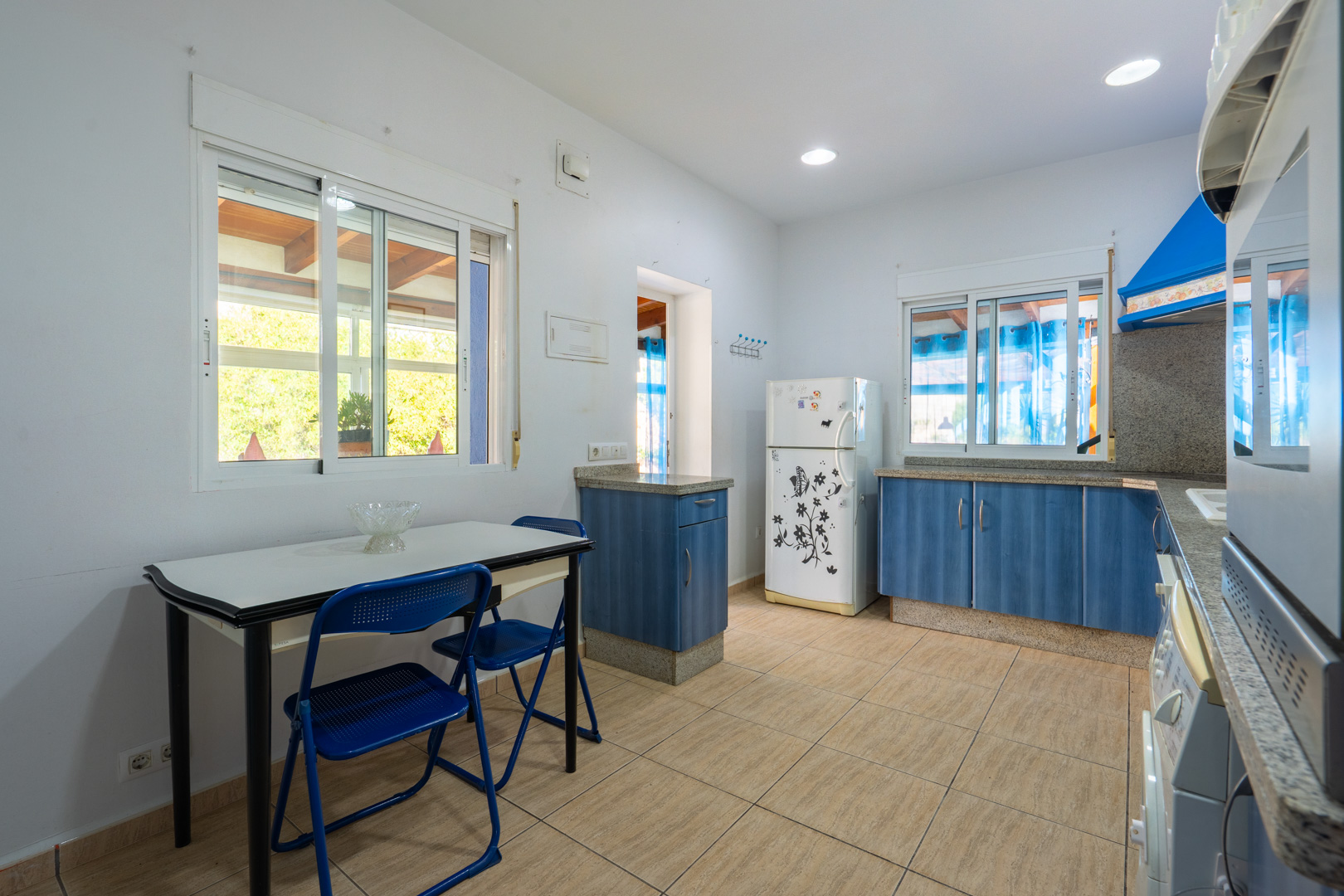 Functional kitchen featuring blue cabinetry, granite countertops, and a breakfast nook. It includes recessed lighting and windows overlooking the covered terrace.