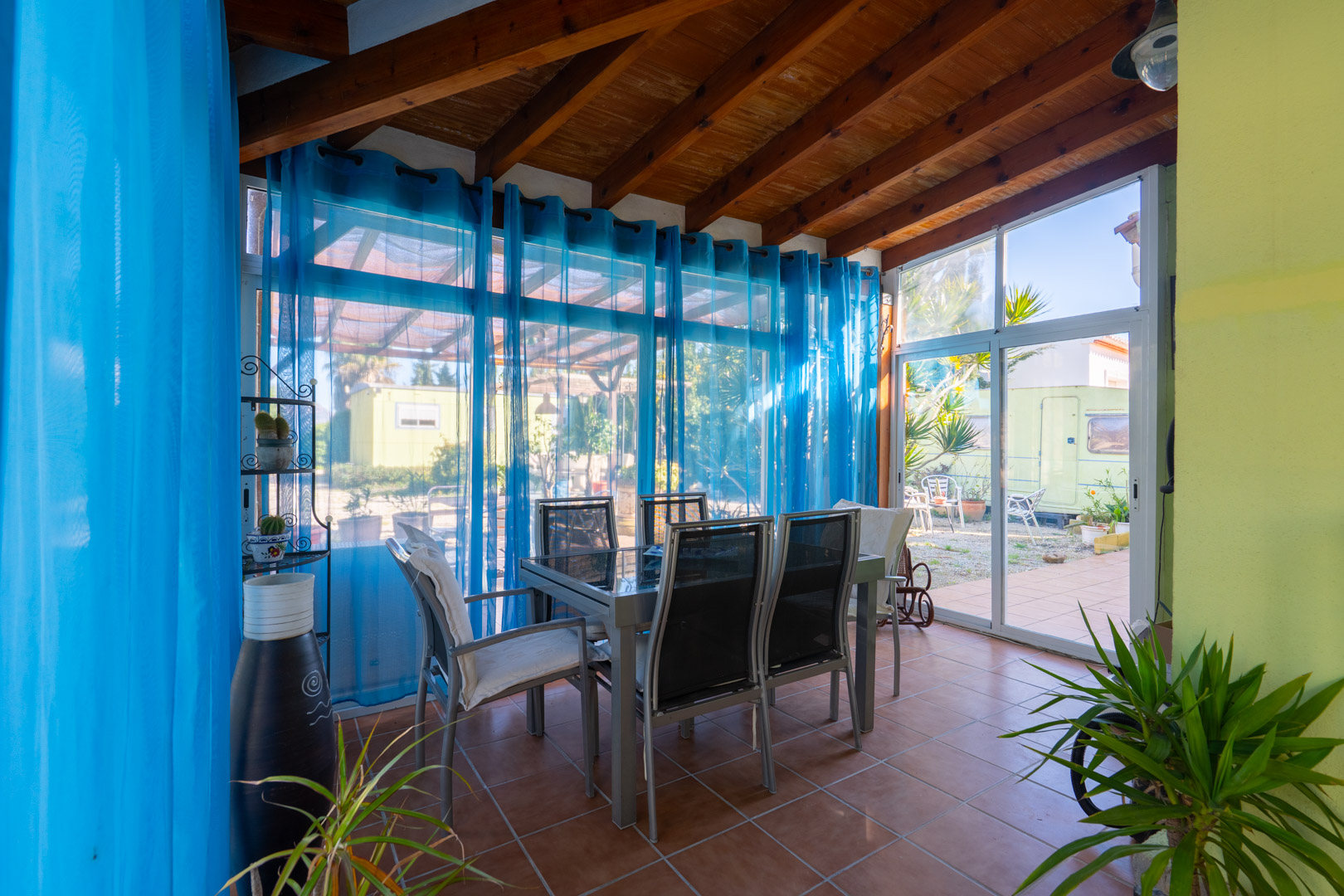 Glazed naya featuring exposed wooden beams, terracotta flooring, and a dining area with direct access to the garden and exterior views.