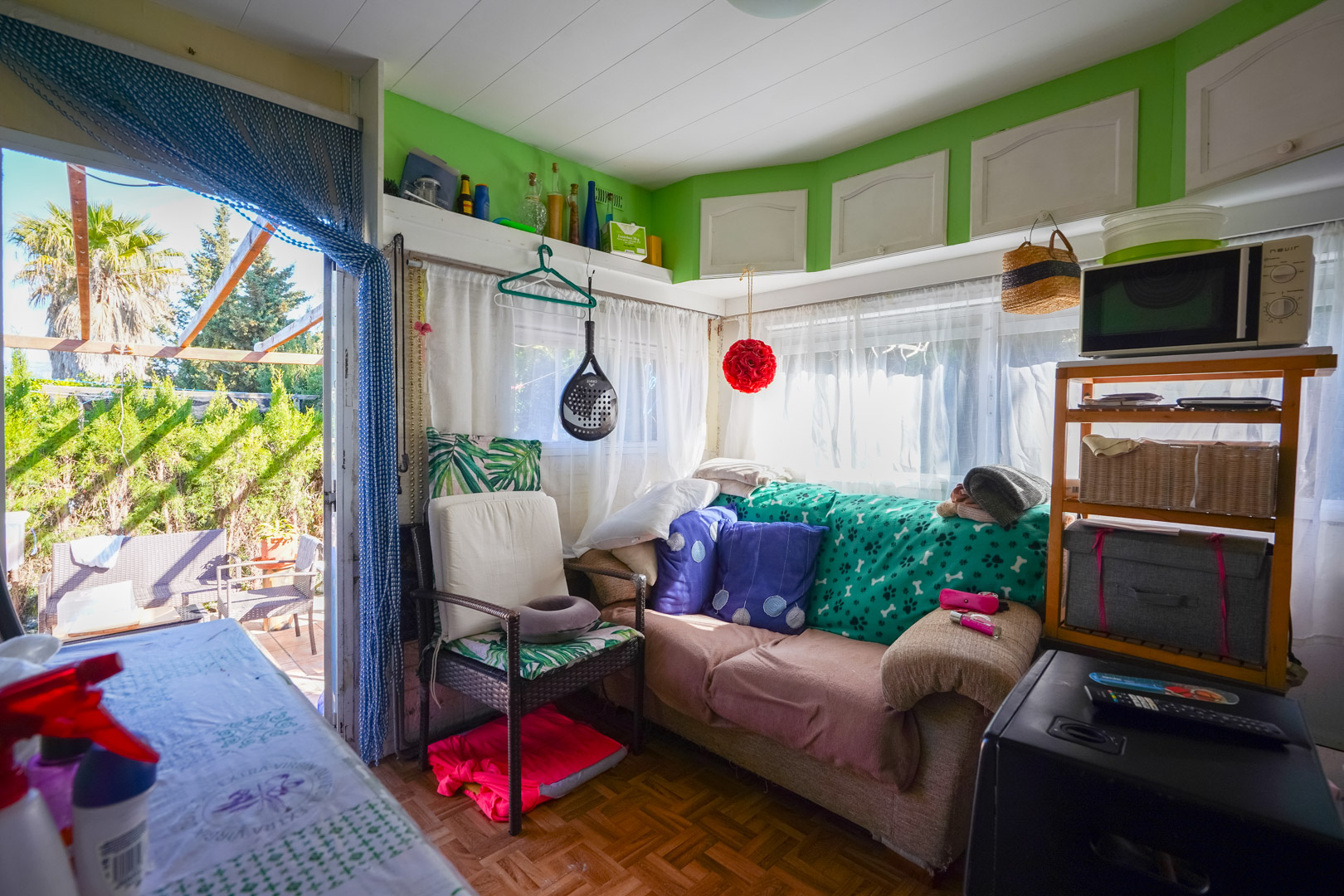 Living area of the prefabricated guest house featuring parquet flooring, natural light through sheer curtains, and direct access to the outdoor patio.