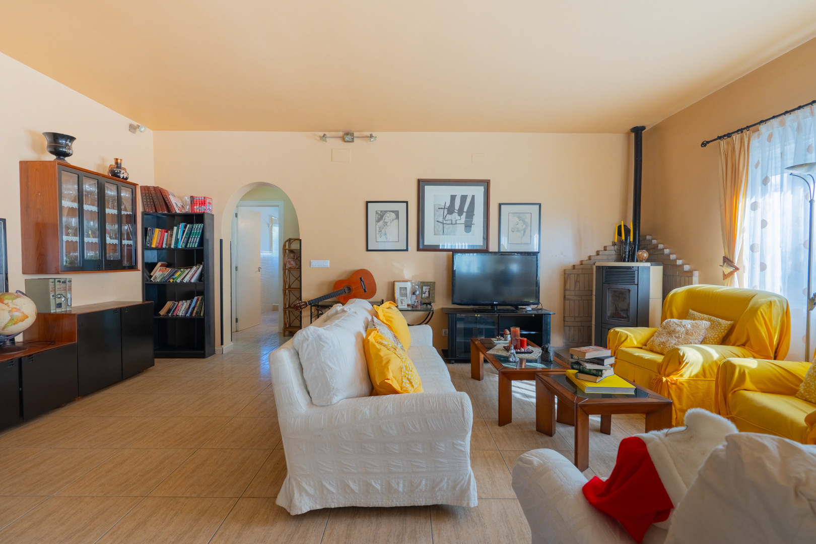 Spacious traditional living room featuring a wood-burning stove, ceramic tile flooring, and a characteristic arched doorway to the hallway.