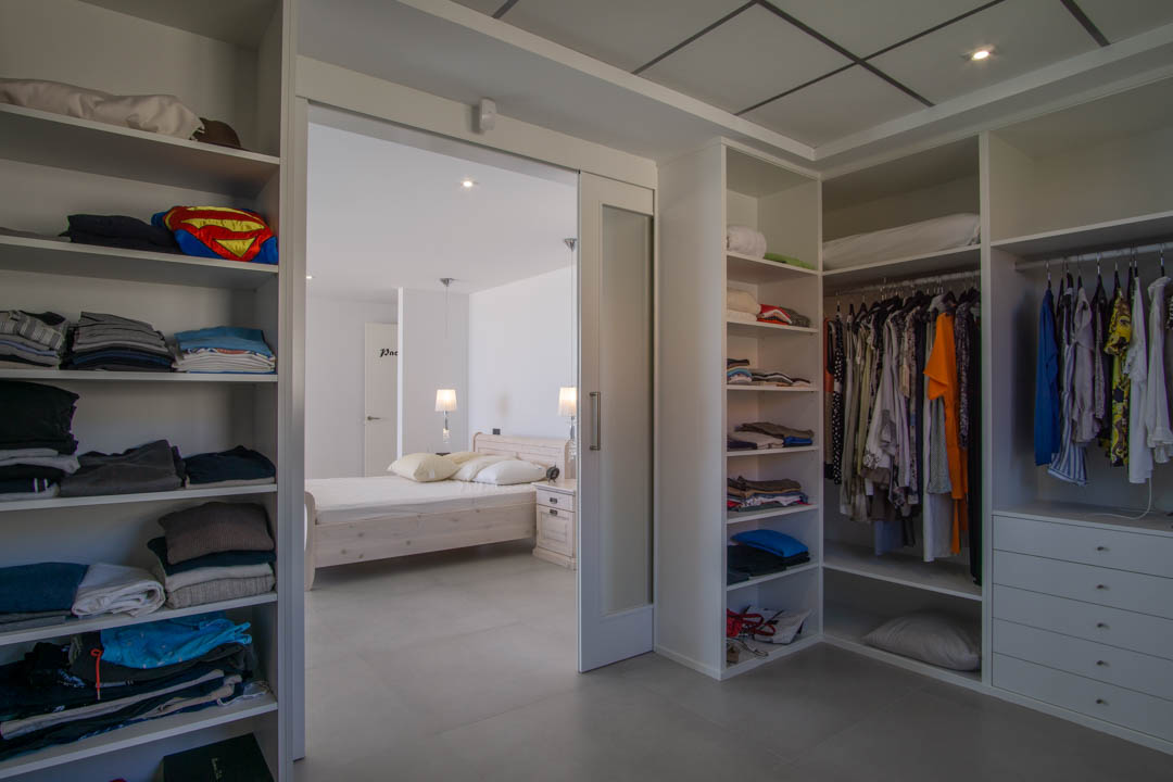 A 12m2 walk-in closet featuring white modular shelving, integrated drawers, and a sliding glass door that opens into the master bedroom.