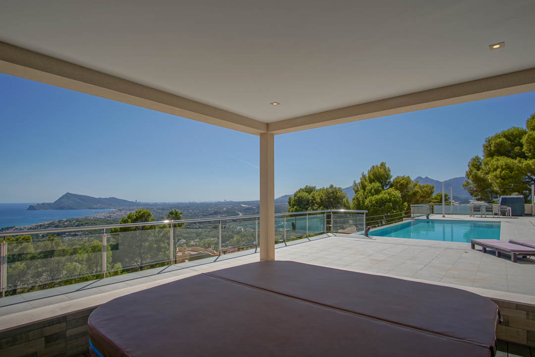 Covered terrace featuring a built-in jacuzzi and panoramic views of the Altea bay, adjacent to a large swimming pool with glass railings.