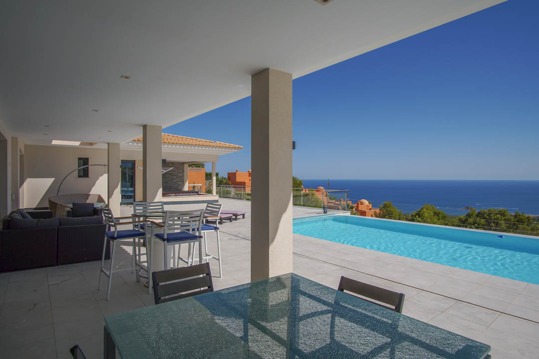 Covered terrace featuring light stone tiling, outdoor dining area, and an infinity pool with panoramic Mediterranean Sea views.