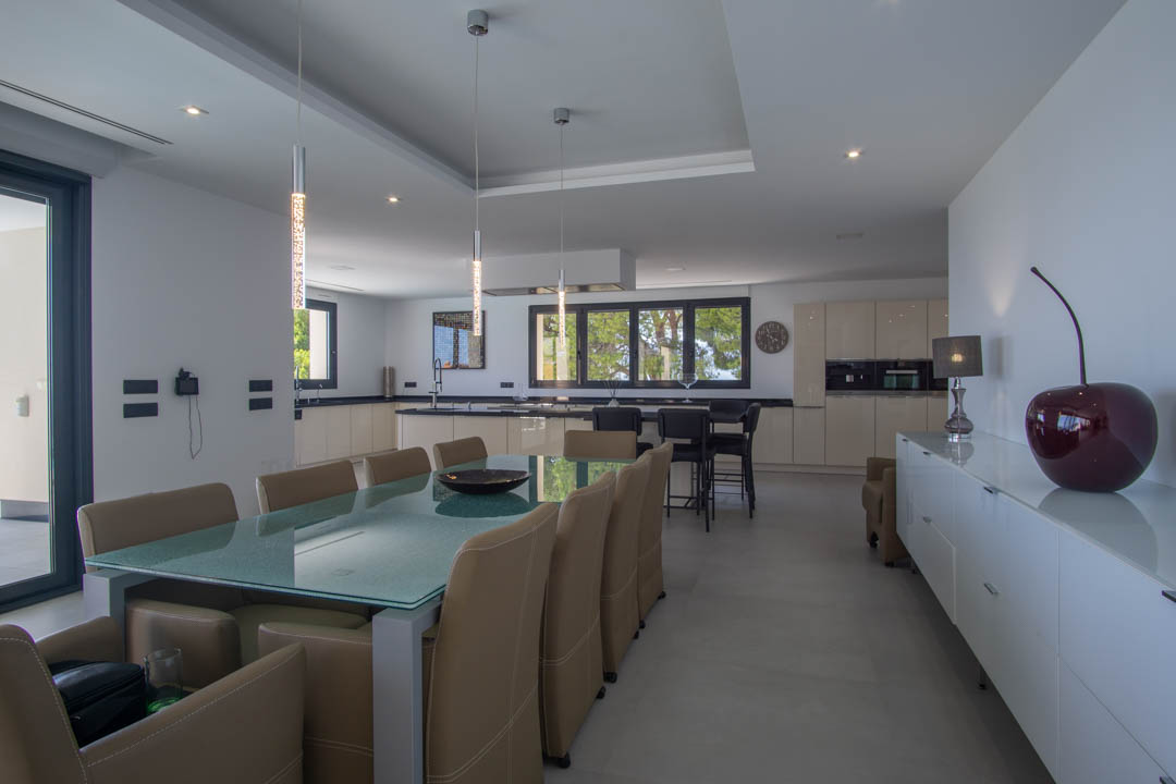 Designer dining area with a glass table and leather chairs, integrated into an open-plan kitchen with dark countertops and recessed lighting.