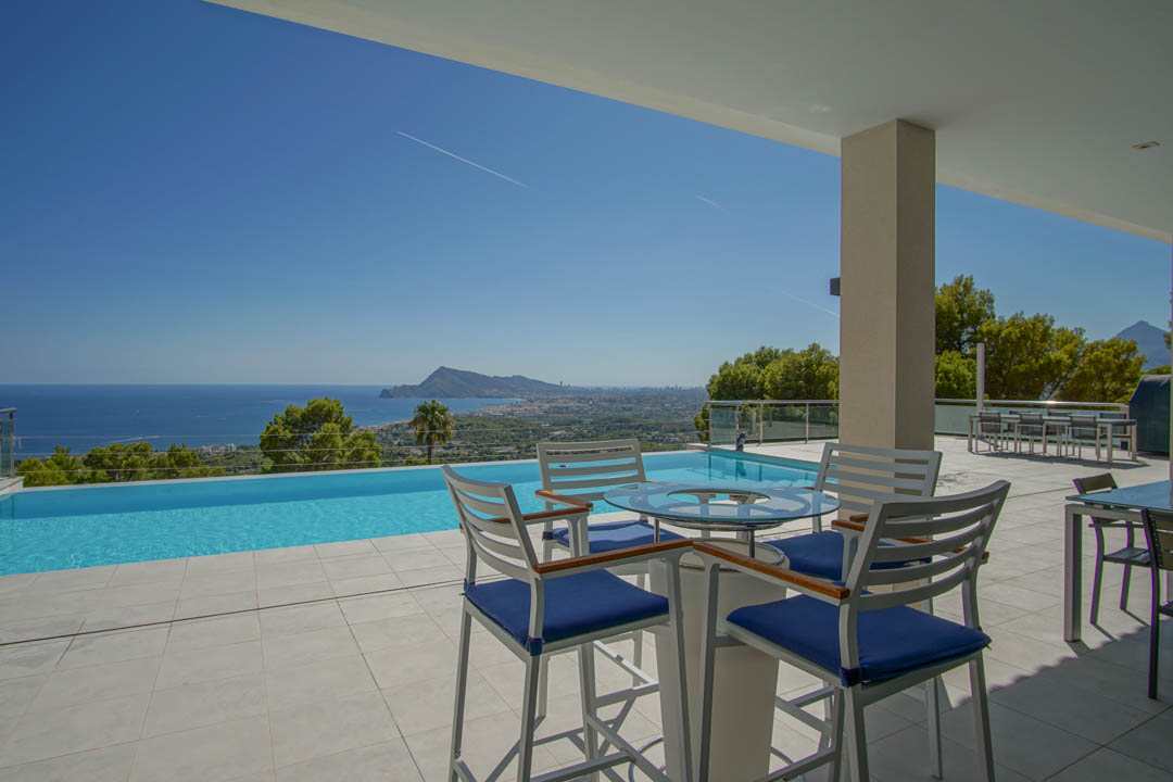 Expansive terrace featuring an infinity pool and panoramic Mediterranean views. The space includes modern high-top seating and seamless white tiling.