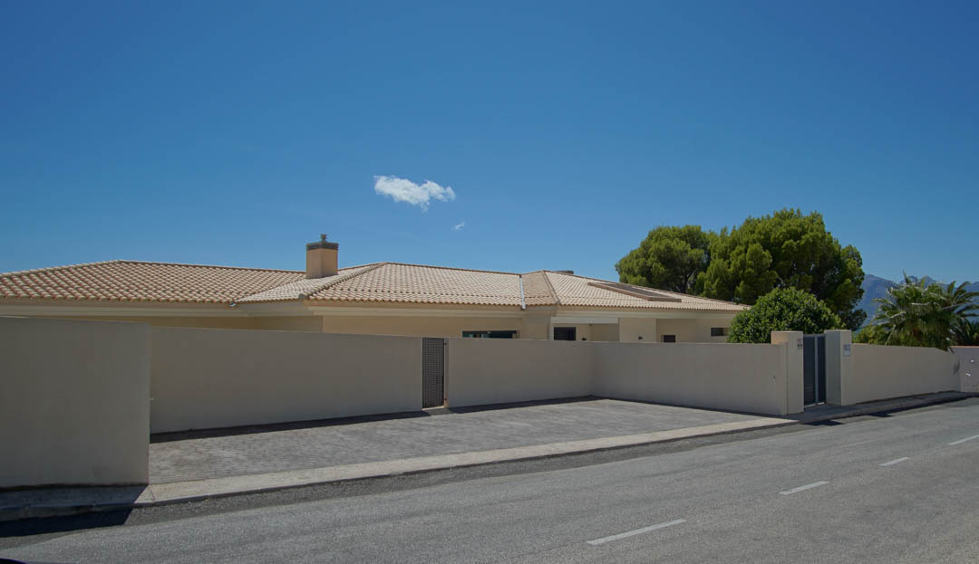 Exterior facade featuring a secure perimeter wall, paved outdoor parking area, and gated entrance under a clear blue sky.