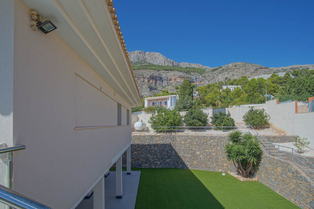 Exterior view of the garden featuring artificial turf, natural stone walls, and a fruit tree area, framed by the Sierra de Altea mountain range.