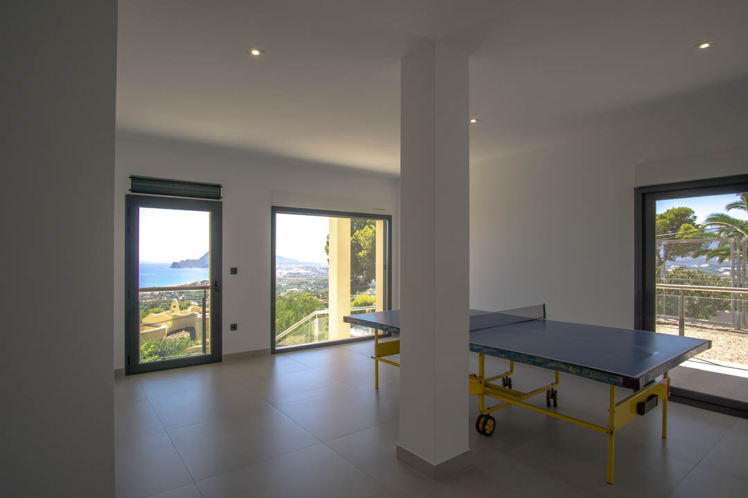 Game room featuring a ping-pong table, grey tiled flooring, and large glass doors showcasing panoramic views of the Mediterranean coastline and Altea bay.