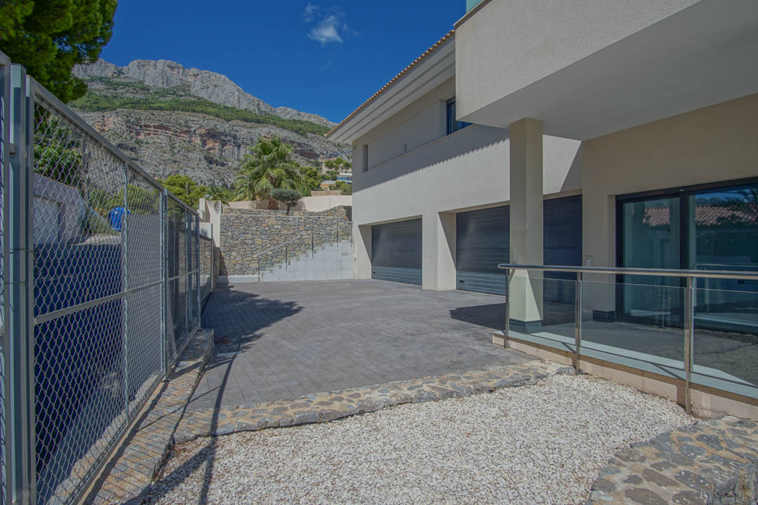 Main entrance featuring a spacious multi-car garage, natural stone walls, and a paved driveway set against the Sierra de Altea mountains.