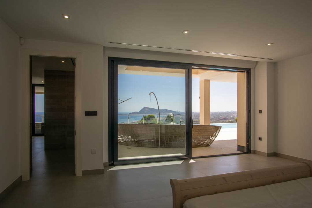 Master bedroom featuring large sliding glass doors that open to a terrace with panoramic sea views, integrated spotlights, and minimalist tile flooring.