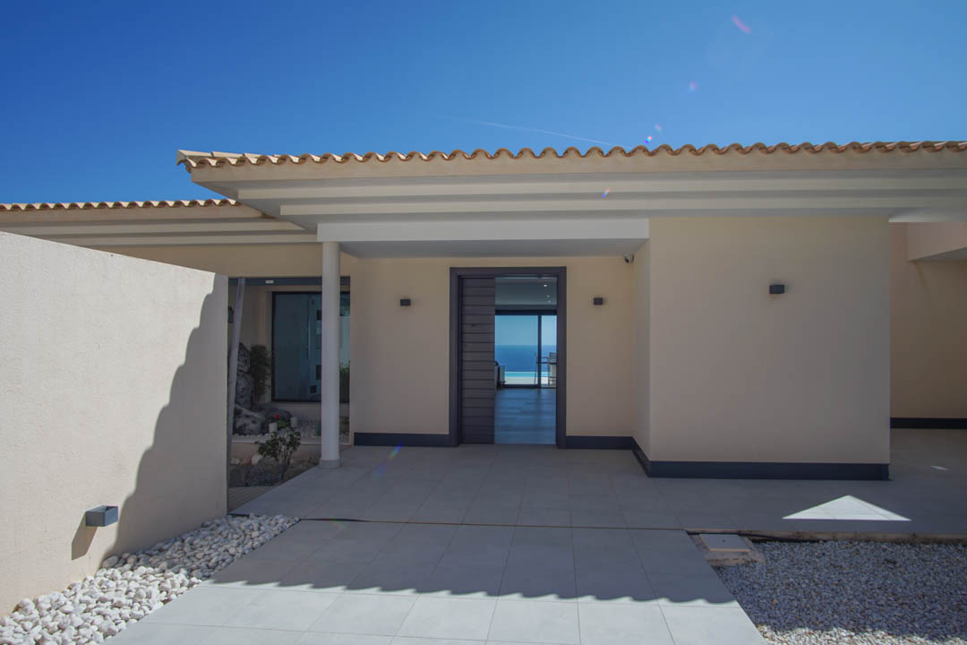 Minimalist main entrance featuring a grey door, tiled porch, and a direct line of sight through the living area to the Mediterranean Sea.