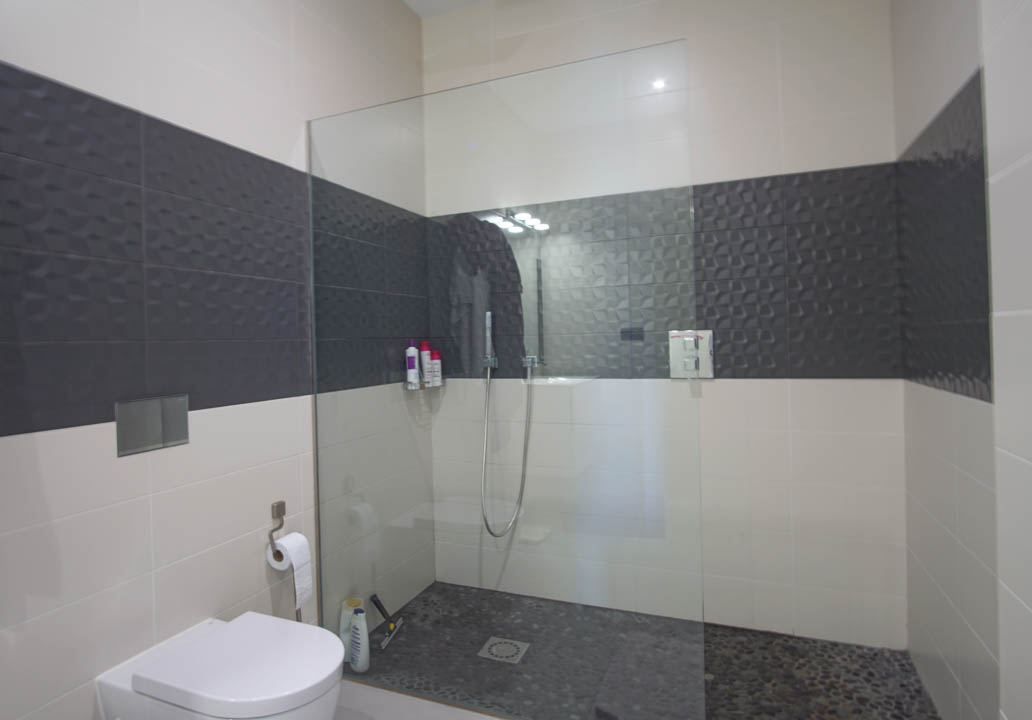 Modern bathroom featuring a walk-in shower with pebble flooring, a fixed glass partition, and textured dark grey accent tiling.