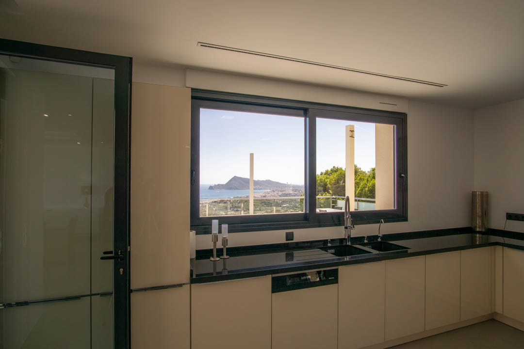 Modern kitchen featuring black granite countertops and a large window with panoramic views of the Altea bay and Mediterranean coastline.