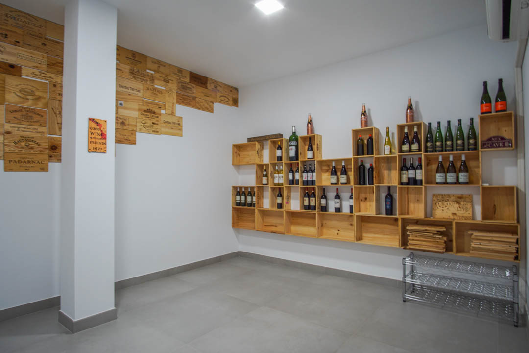 Private wine cellar featuring modular wooden crate shelving and decorative wall panels set against white walls and grey tiled flooring.